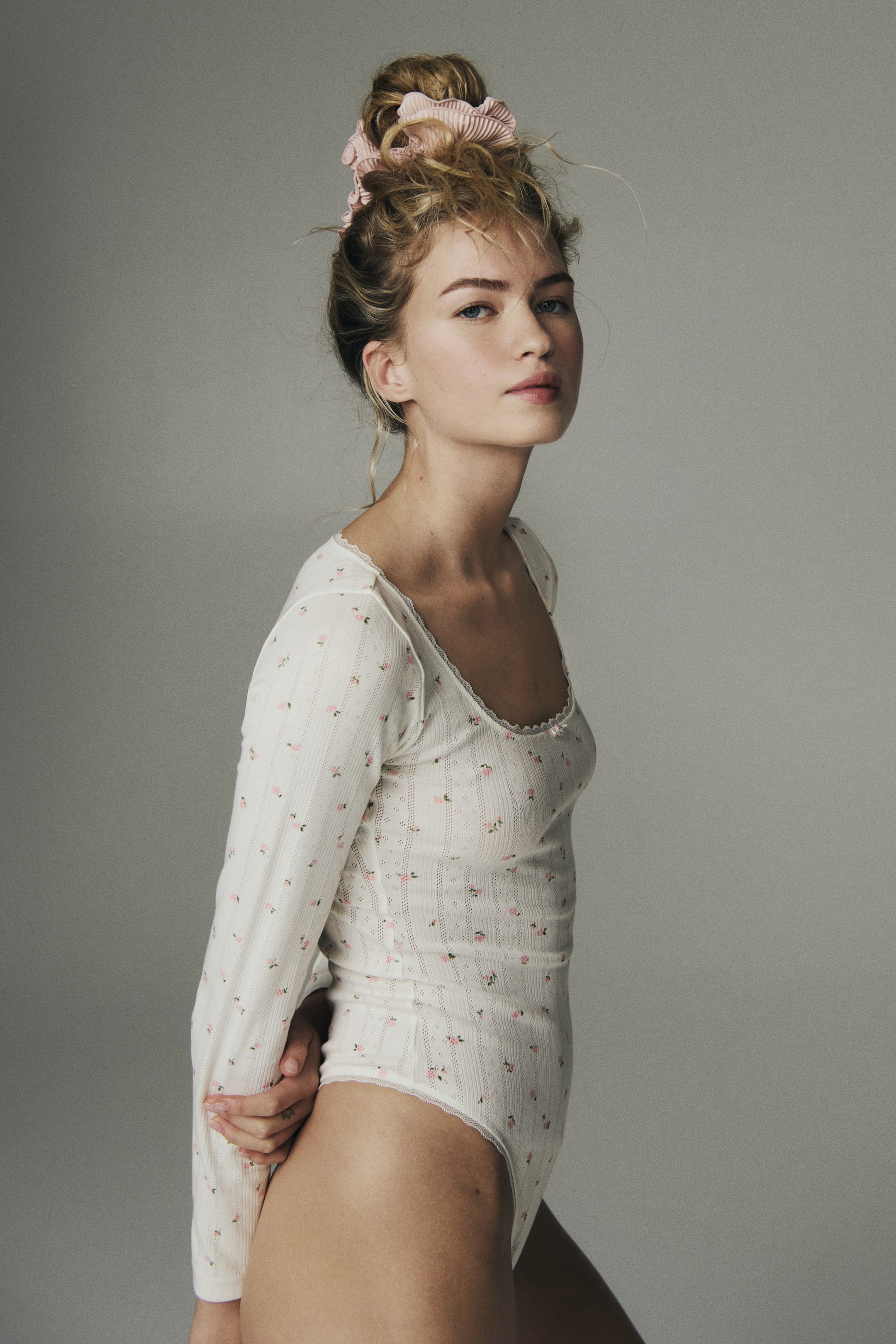 View larger image: A long-sleeved thong body in pointelle-knit cotton jersey, featuring a pink floral pattern and a square neckline with lace trim and a small bow, is worn by the model.