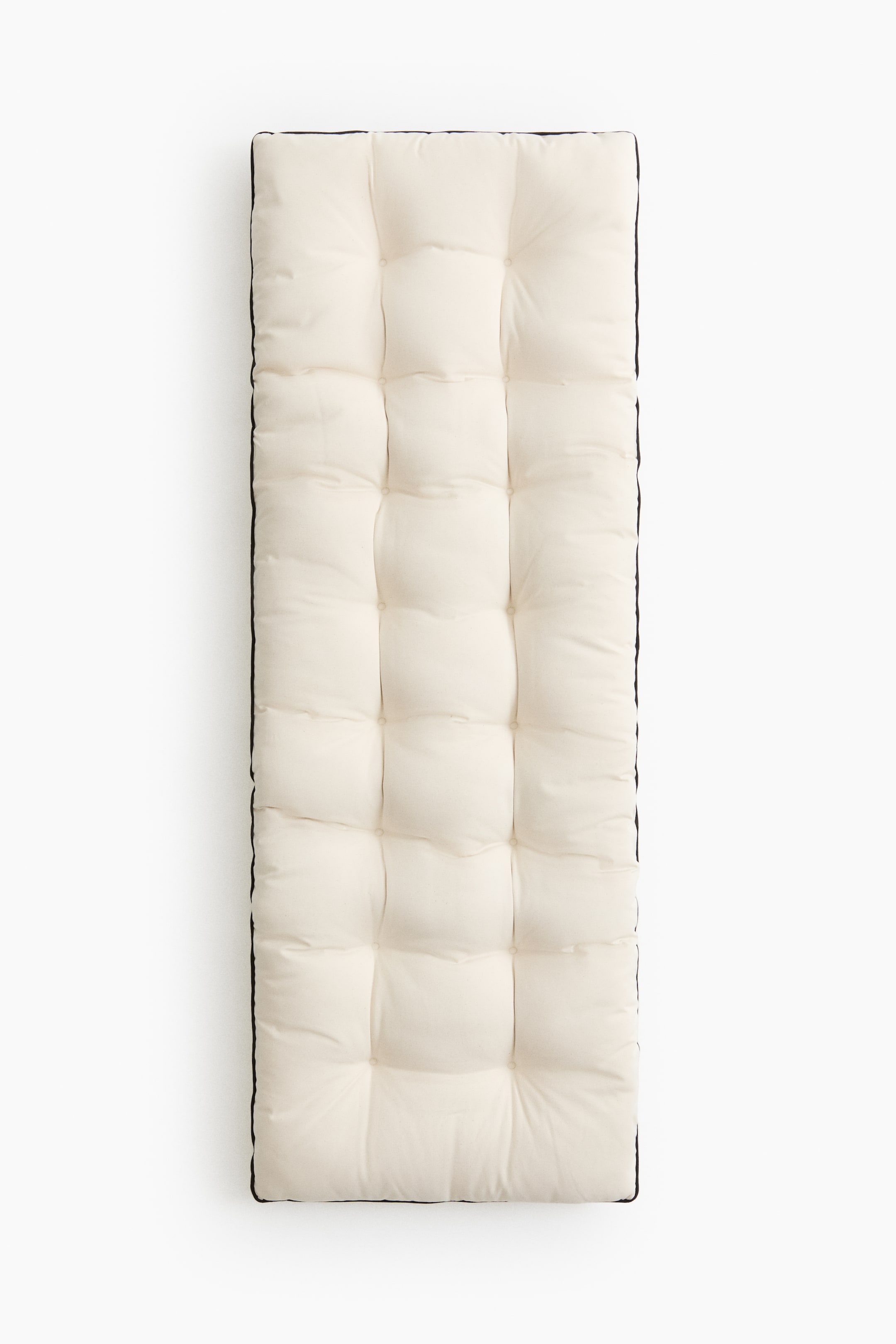 Visa större bild: En off-white rektangulär tuftad kudde visar sin ovansida, som har ett rutmönster skapat av fyrkantiga tufts, var och en med en central fördjupning. Mörk passpoal kantar kuddens omkrets.