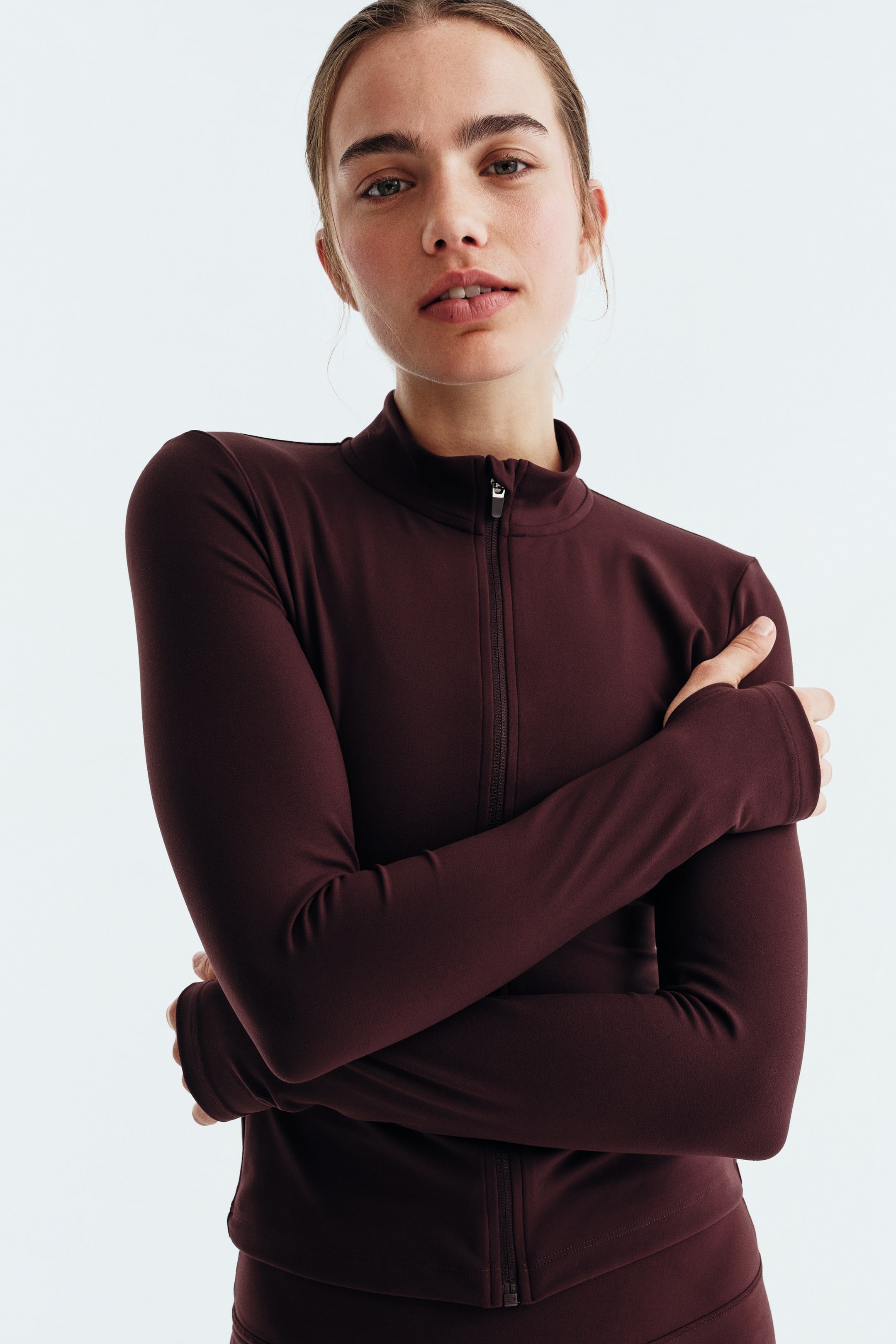 View larger image: A deep maroon long-sleeved top features a full-zip front closure with a silver pull tab and a mock neck collar. Its fitted sleeves extend to the wrists, and the cuffs incorporate thumbholes.