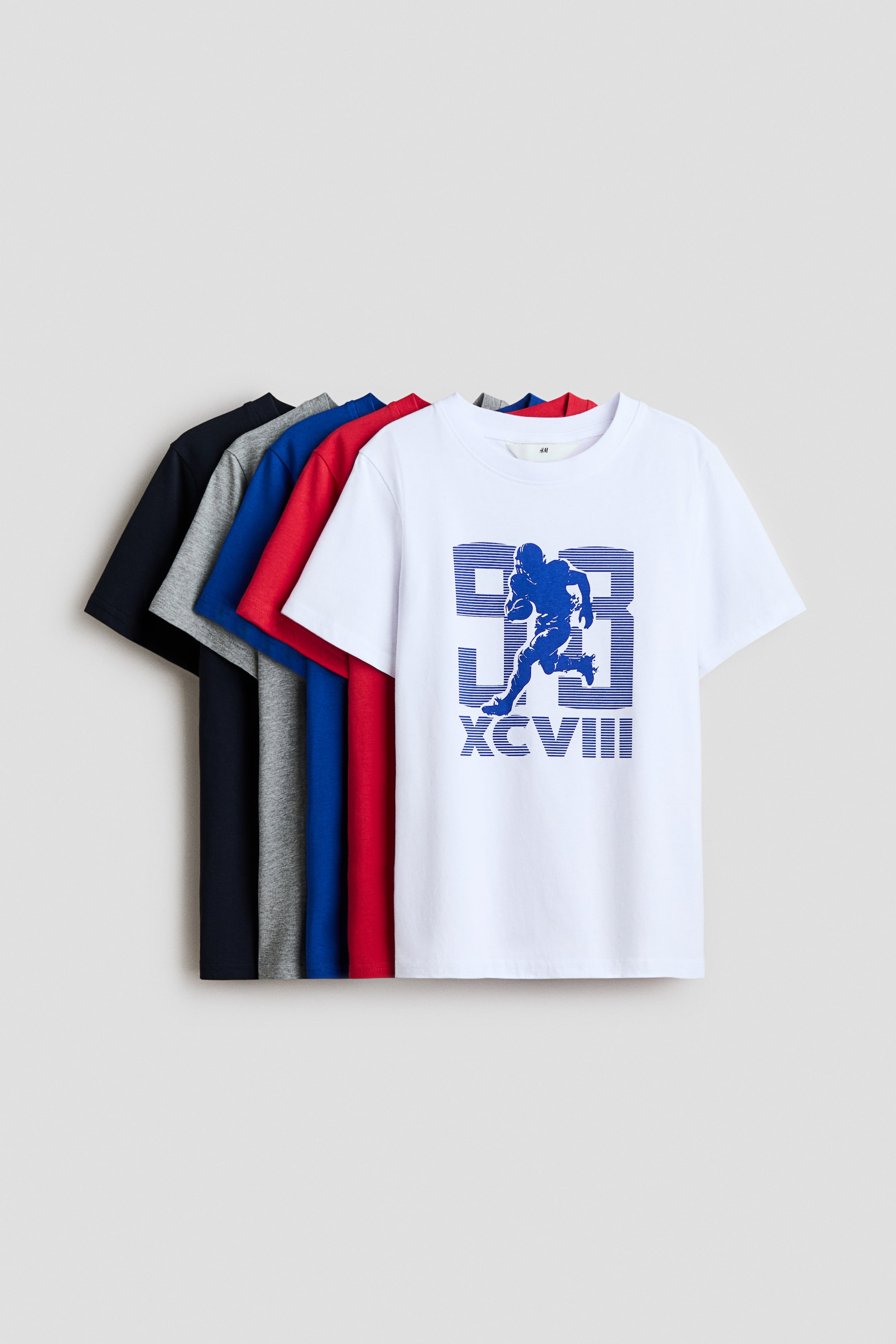 View larger image: Five t-shirts are showcased in a layered arrangement, highlighting a range of colors such as navy blue, gray, royal blue, red, and white. The front white t-shirt features a blue graphic of a football player with '93' and 'XCVIII', and all t-shirts boast a round, rib-trimmed neckline.