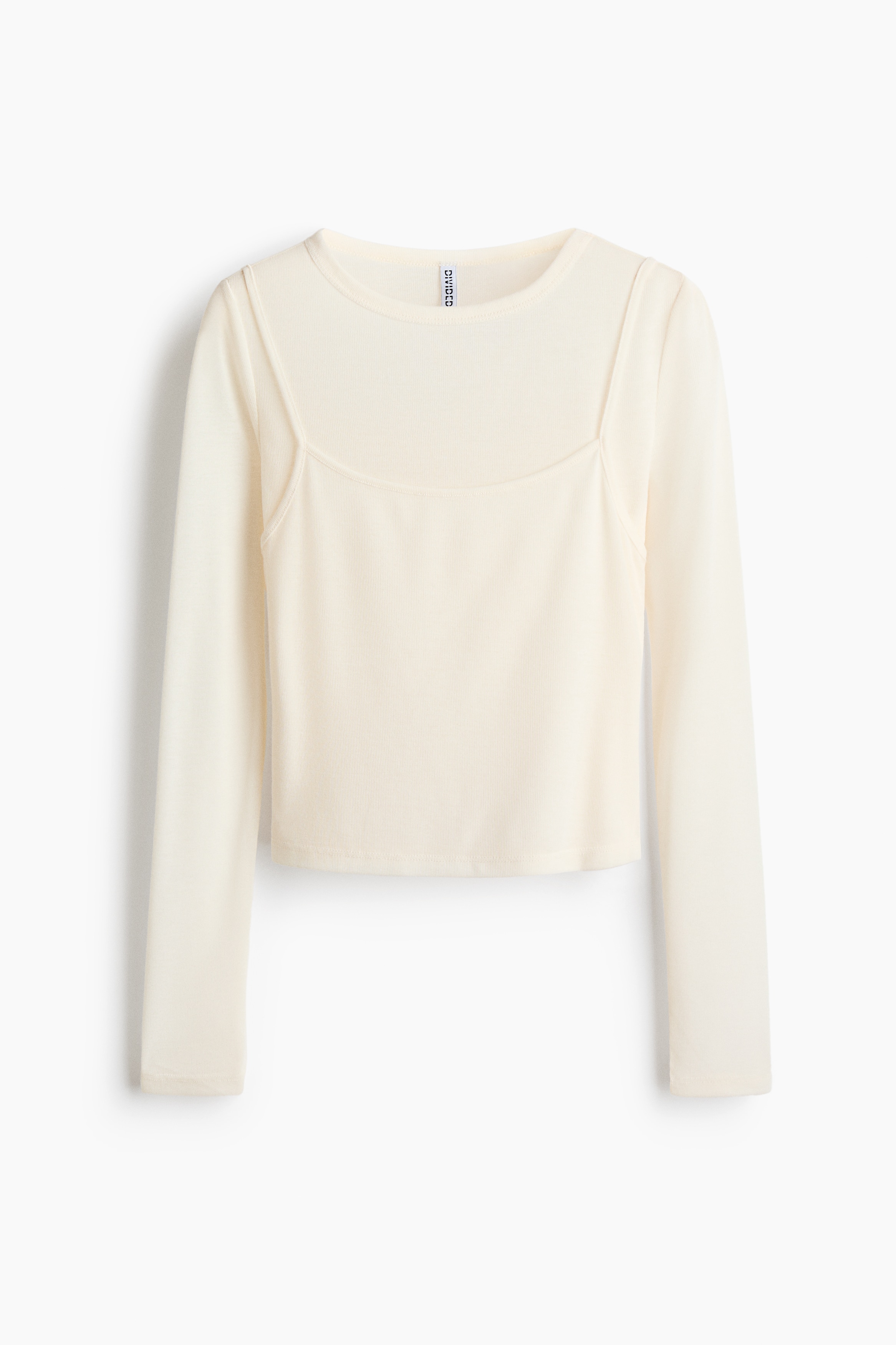 A layered, long-sleeve jersey top featuring a round-neck underlayer and a scoop-neck outer layer with narrow shoulder straps is being worn by the model. The model is styling the top with low-rise jeans, posing with hands resting in the pockets.
