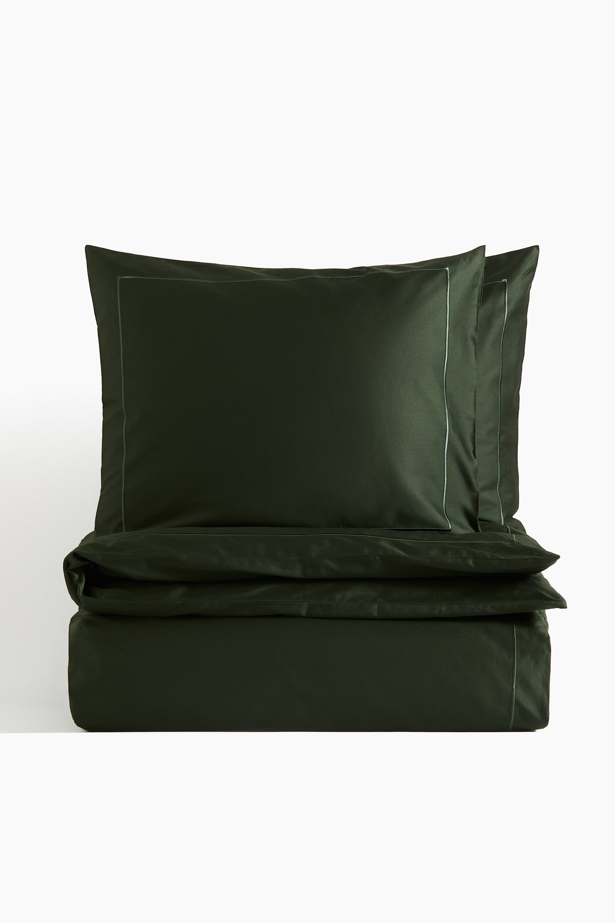Agrandir l'image: Un ensemble de housse de couette vert foncé est présenté, comprenant deux taies d’oreiller empilées et une housse de couette pliée. Chaque article présente un discret passepoil de couleur plus claire le long de ses bords, formant un liseré.