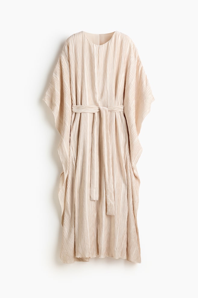 Un vestido caftán crema presenta una textura arrugada en su totalidad, mostrando su PARTE DELANTERA. Un cinturón a juego con lazada se ajusta a la cintura, creando pliegues suaves, y mangas anchas e integradas caen desde los hombros. - 1