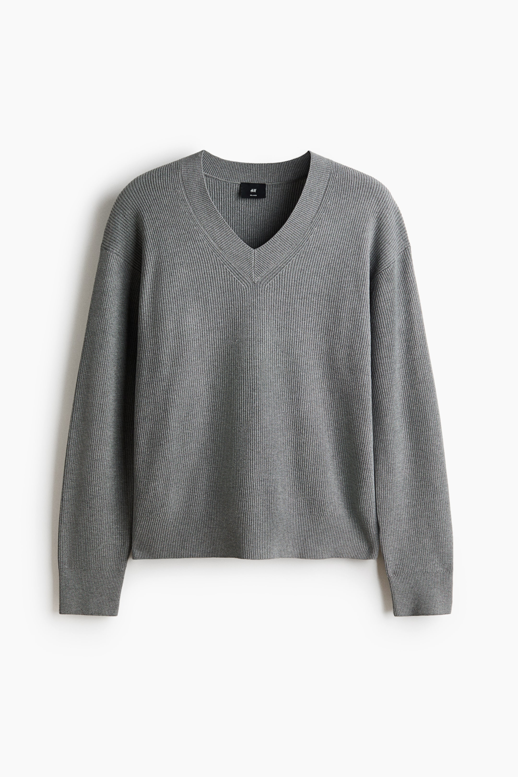 Visualizza immagine più grande: Un maglione grigio con scollo a V è mostrato frontalmente, mettendo in risalto una texture a coste verticali prominente su tutta la superficie. Presenta uno scollo a V, maniche lunghe e un orlo dritto.