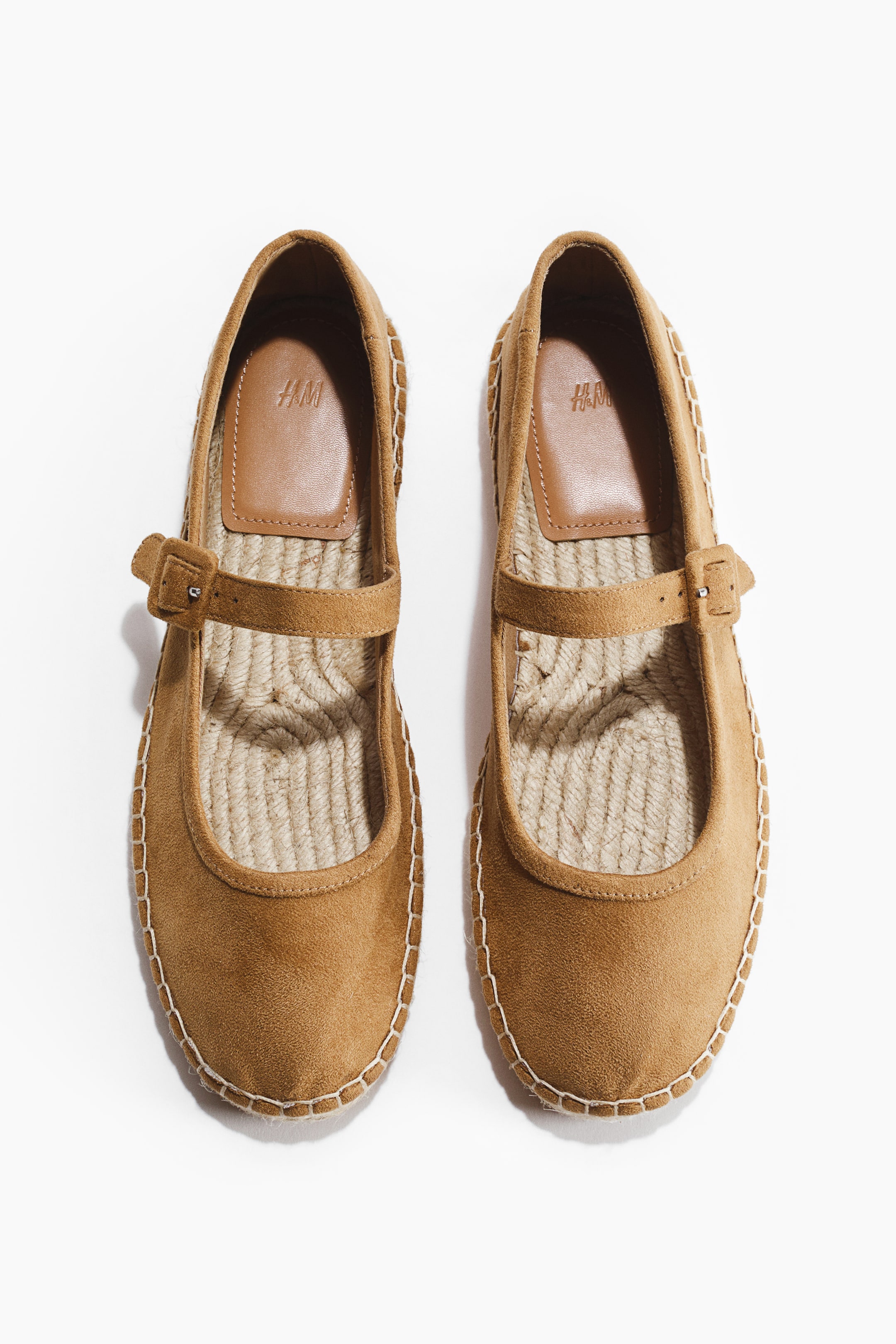 Vis større bilde: Et par beige espadrillos fra H&M med avrundede tupper og en justerbar stropp over fronten. Flettet jute pryder sålene og danner fotbedene, mens hvite sømmer detaljerer kantene på de semsket-lignende overdelene.