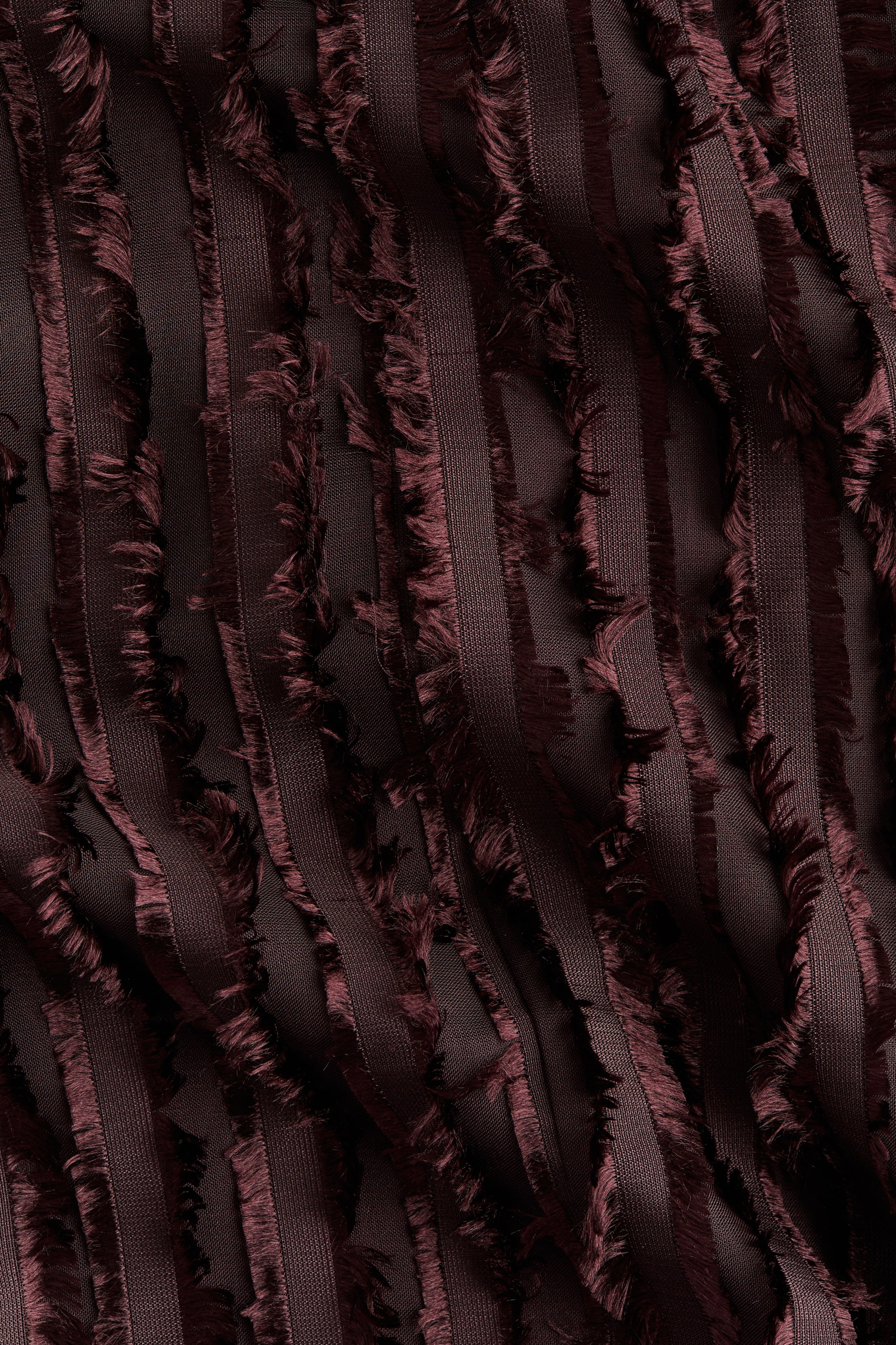Ver imagen más grande: La tela es un material de color marrón rojizo oscuro con franjas verticales alternas de textura suave y tejida, y un fleco deshilachado pronunciado. Esta tela dimensional está sutilmente drapeada, revelando una capa base transparente entre los elementos texturizados.
