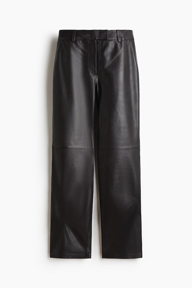 Ce pantalon droit en cuir noir est présenté de face, avec une taille ajustée munie de passants pour ceinture et une fermeture frontale dissimulée. Une couture horizontale distinctive traverse les deux jambes au niveau des genoux, soulignant la silhouette structurée. - 1