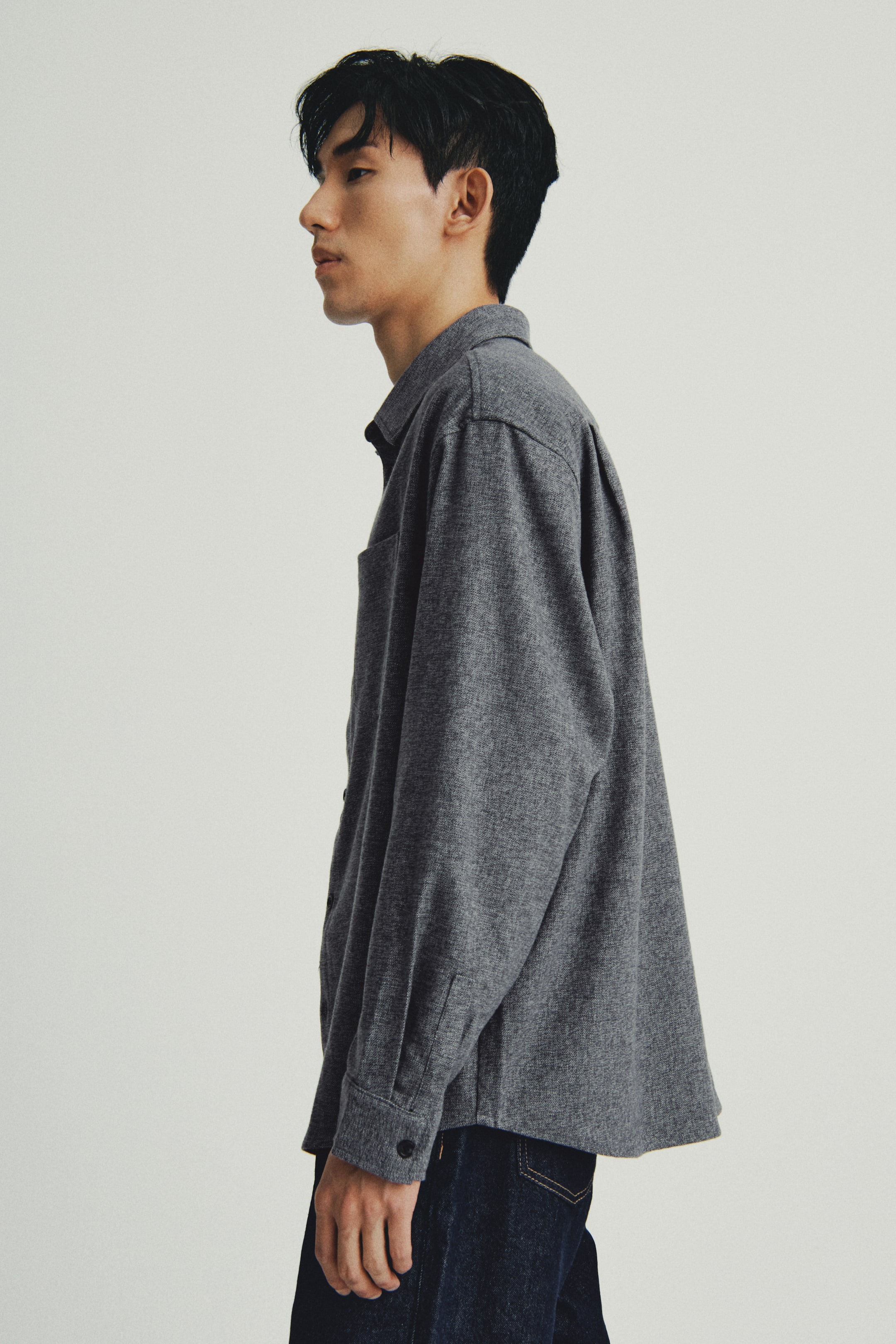 이미지 확대 보기: 회색 헤더 오버셔츠는 옆모습으로 제시되며, 뾰족 칼라, 단일 가슴 포켓, 긴 소매와 단추 커프스가 특징입니다. 여유로운 핏은 진한 파란색 청바지 바로 위에 맞아떨어집니다.