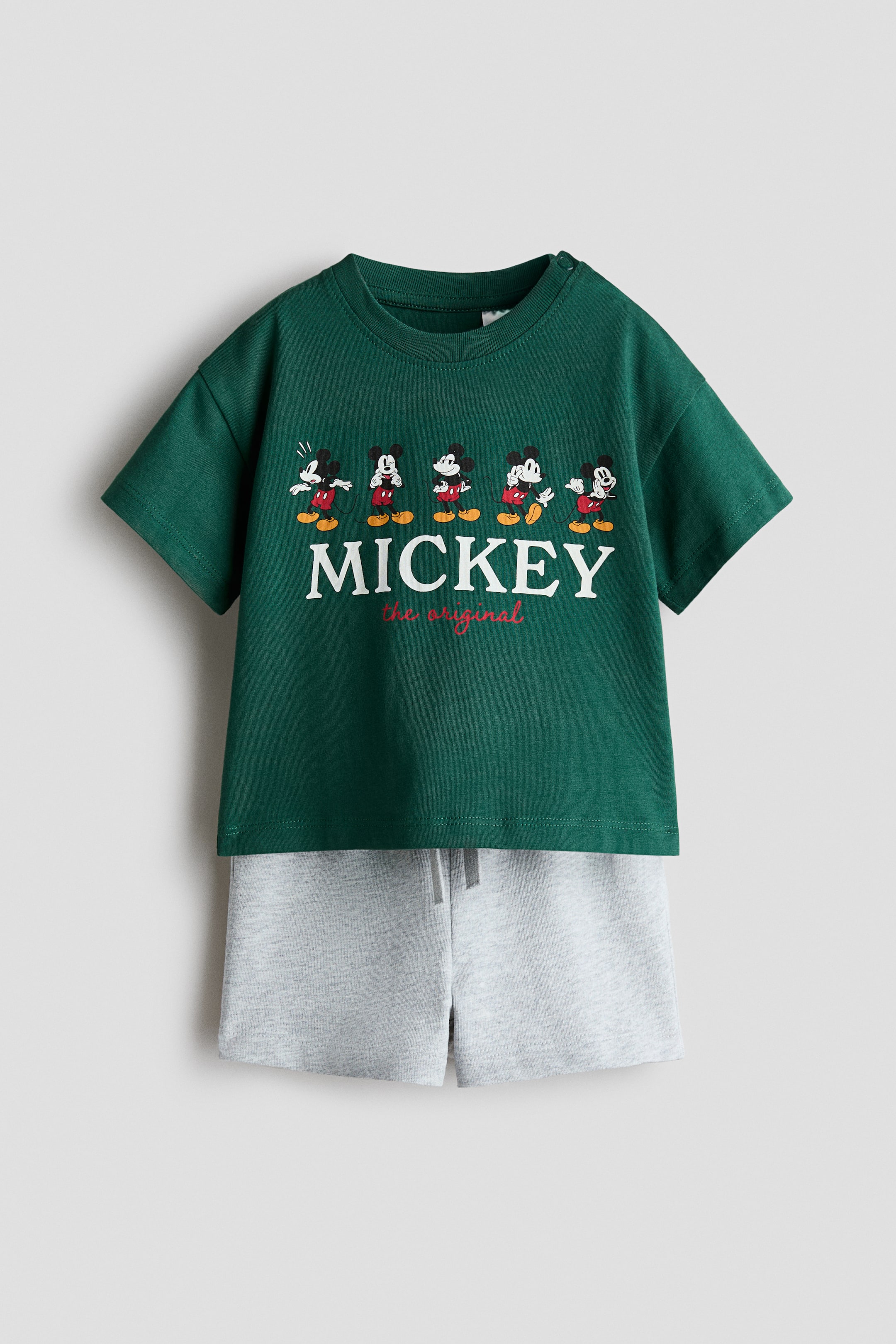 View larger image: The 2-piece printed set, shown front-facing, features a dark green short-sleeved T-shirt and light grey heathered shorts. The T-shirt displays five Mickey Mouse figures above the word ‘MICKEY’ and the text ‘the original’, with a ribbed crew neck and shoulder snap buttons, while the shorts are designed with an elasticated drawstring waistband.