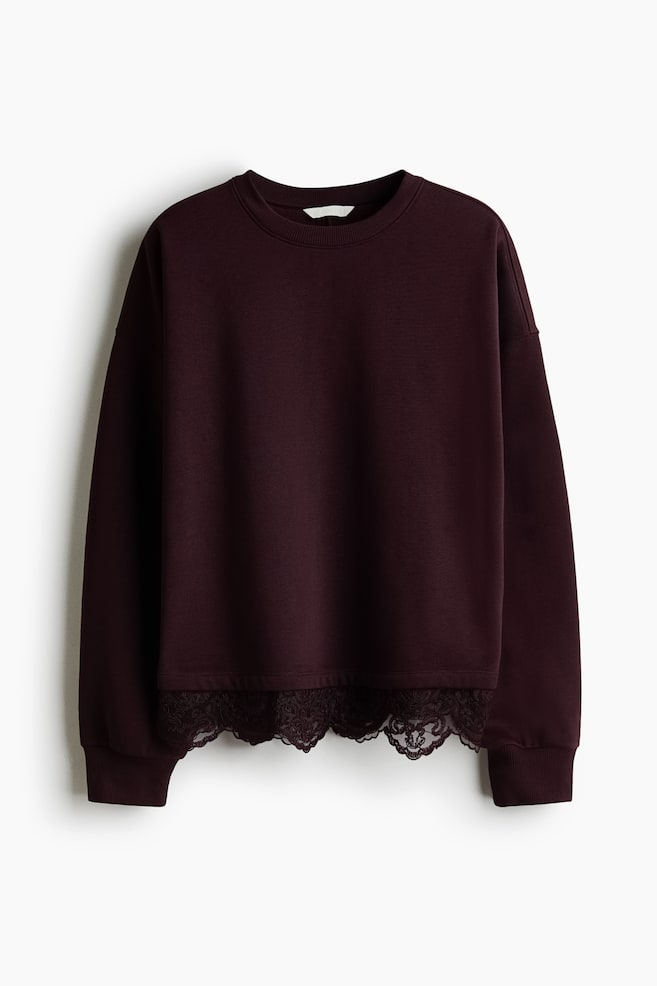 A dark burgundy sweatshirt is facing front, featuring a ribbed crew neck, dropped shoulders, and long sleeves with ribbed cuffs. The hem is embellished with a matching, semi-sheer scalloped floral lace trim. - 1