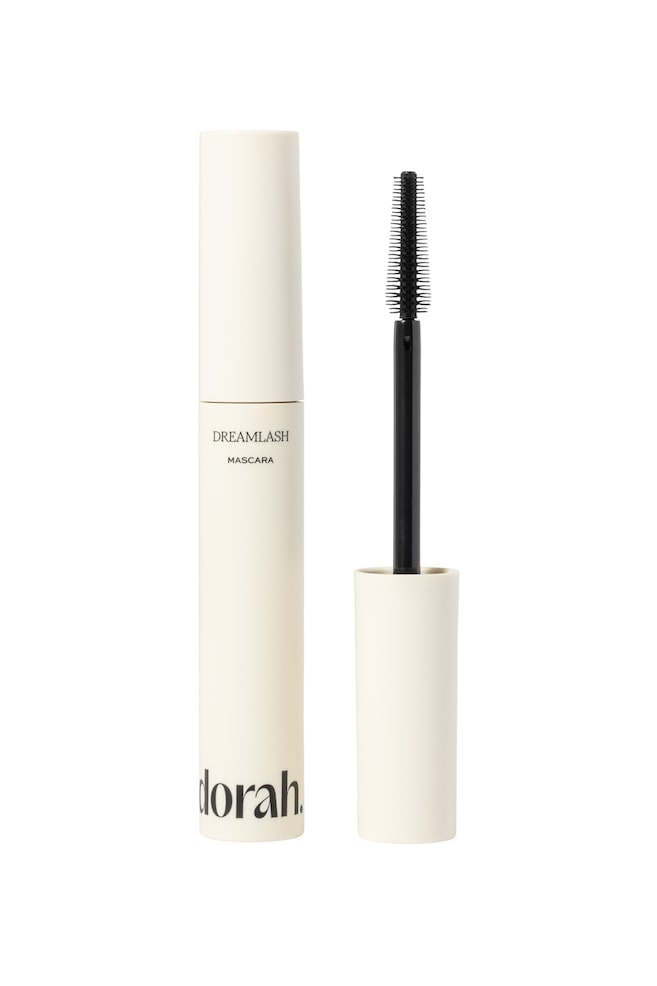 Et lys cremefarvet mascararør står oprejst og viser teksten "DREAMLASH MASCARA" på forsiden. Dens sorte spiralbørste står lodret ved siden af, fjernet fra røret. - 1