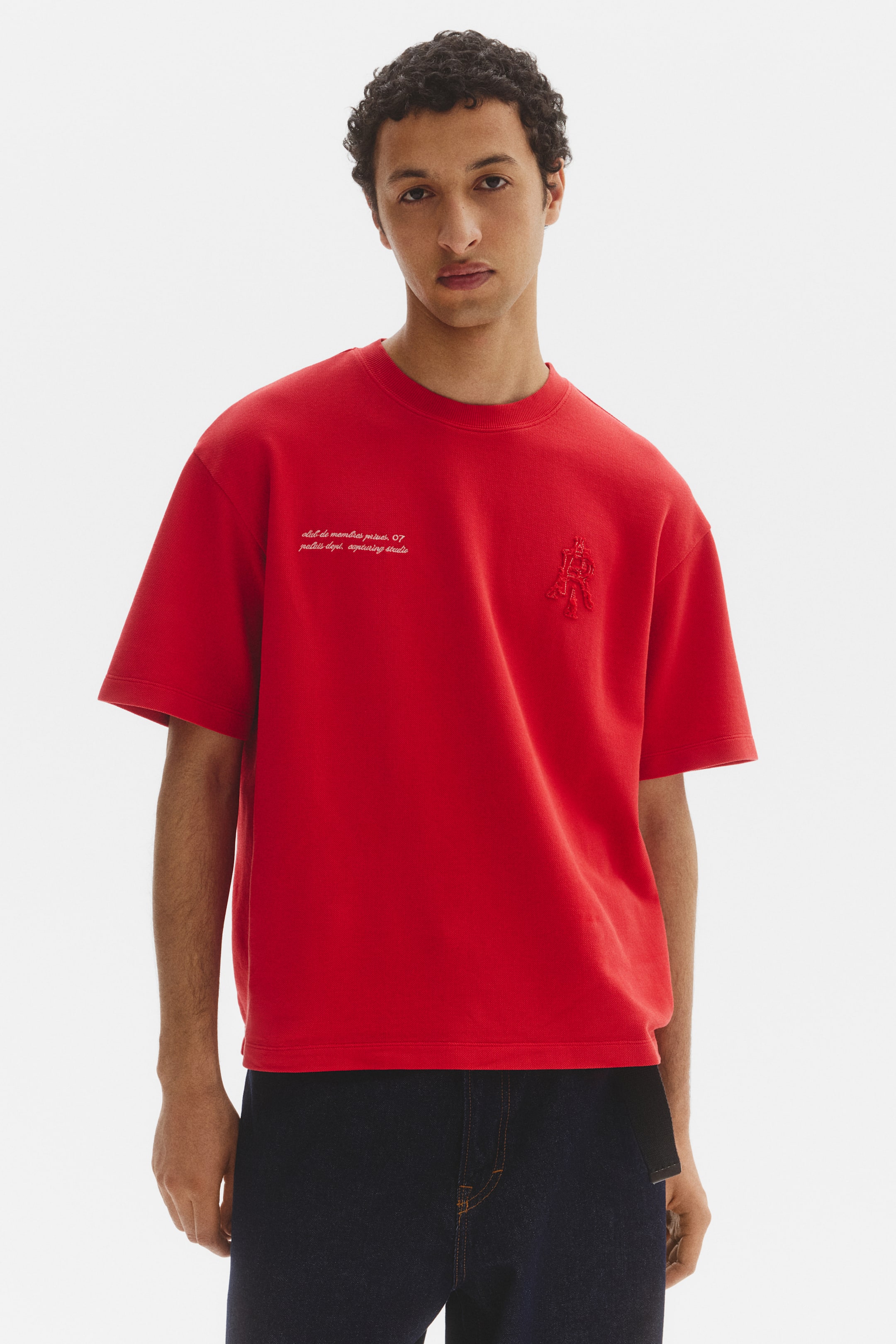 View larger image: This red t-shirt showcases a crew neck design and short sleeves. It features white embroidered text on the left chest and a red embroidered emblem on the right chest, presented from a front-facing angle.