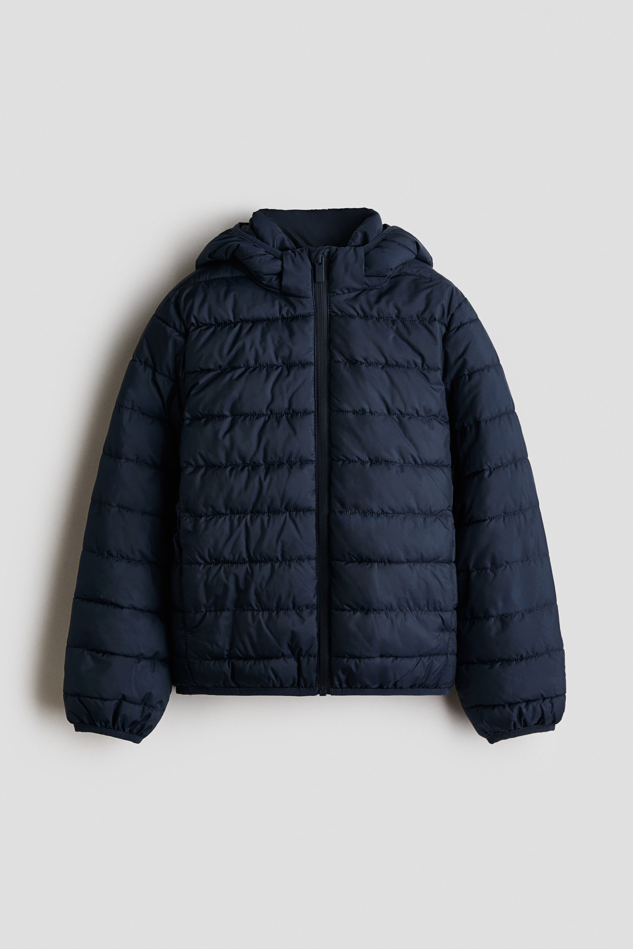 Agrandir l'image: Une veste matelassée bleu foncé est présentée de face, mettant en valeur des coutures horizontales sur le corps et les manches. Elle est dotée d'une fermeture éclair frontale sur toute la longueur, d'un col montant, d'une capuche et de finitions élastiquées aux poignets et à l'ourlet.