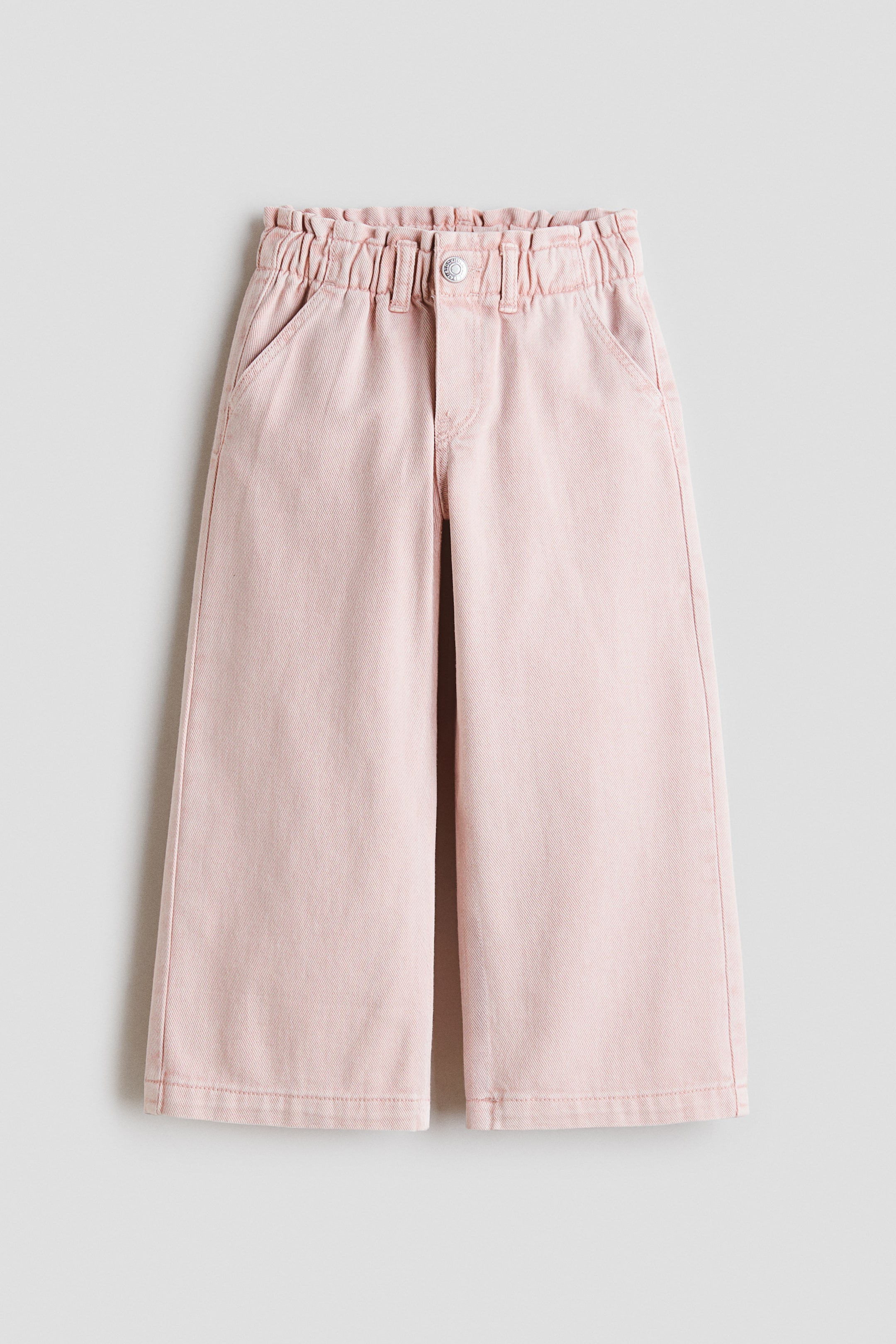 View larger image: Pink cotton denim jeans are shown from the front, featuring wide legs and an elasticated paper-bag waist. They have a faux fly with a button and diagonal side pockets.