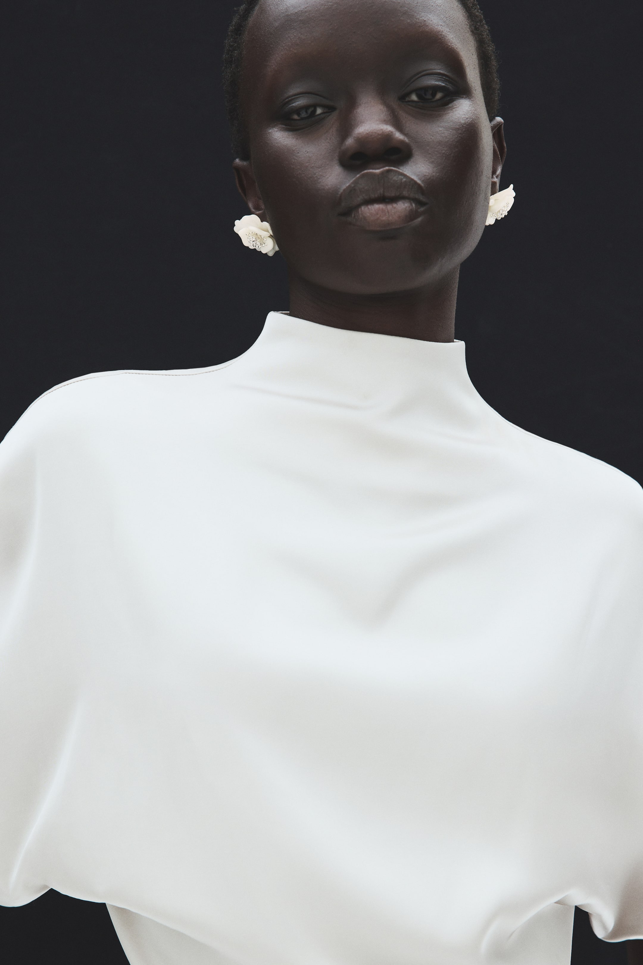 View larger image: Plastic flower-shaped earrings, featuring sparkling rhinestones at their centres, are being worn by the model, complementing her white, high-neck top.
