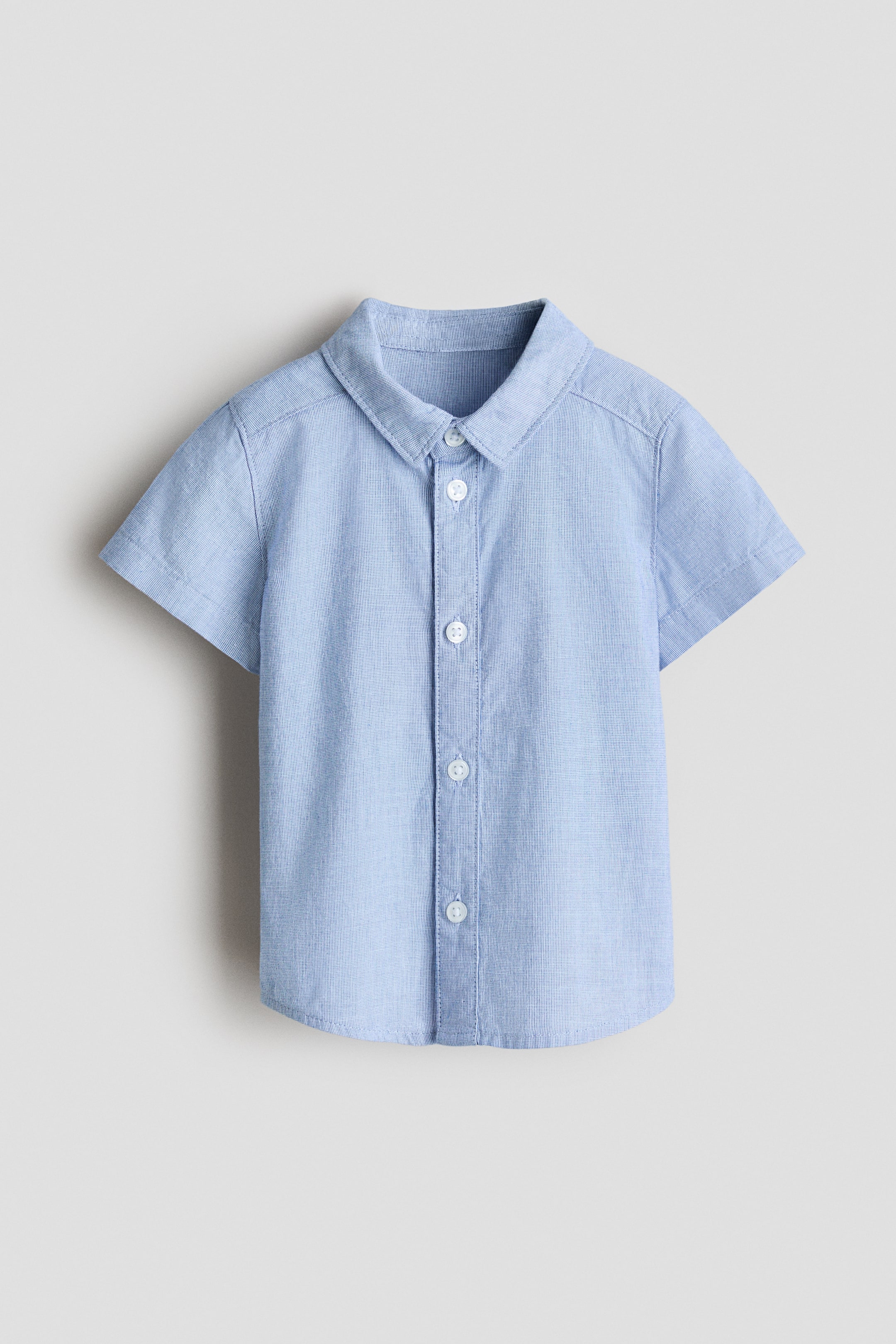 View larger image: A light blue short-sleeved shirt made of crisp cotton poplin is shown from the front. It features a turn-down collar, white buttons down the front, and a gently rounded hem.