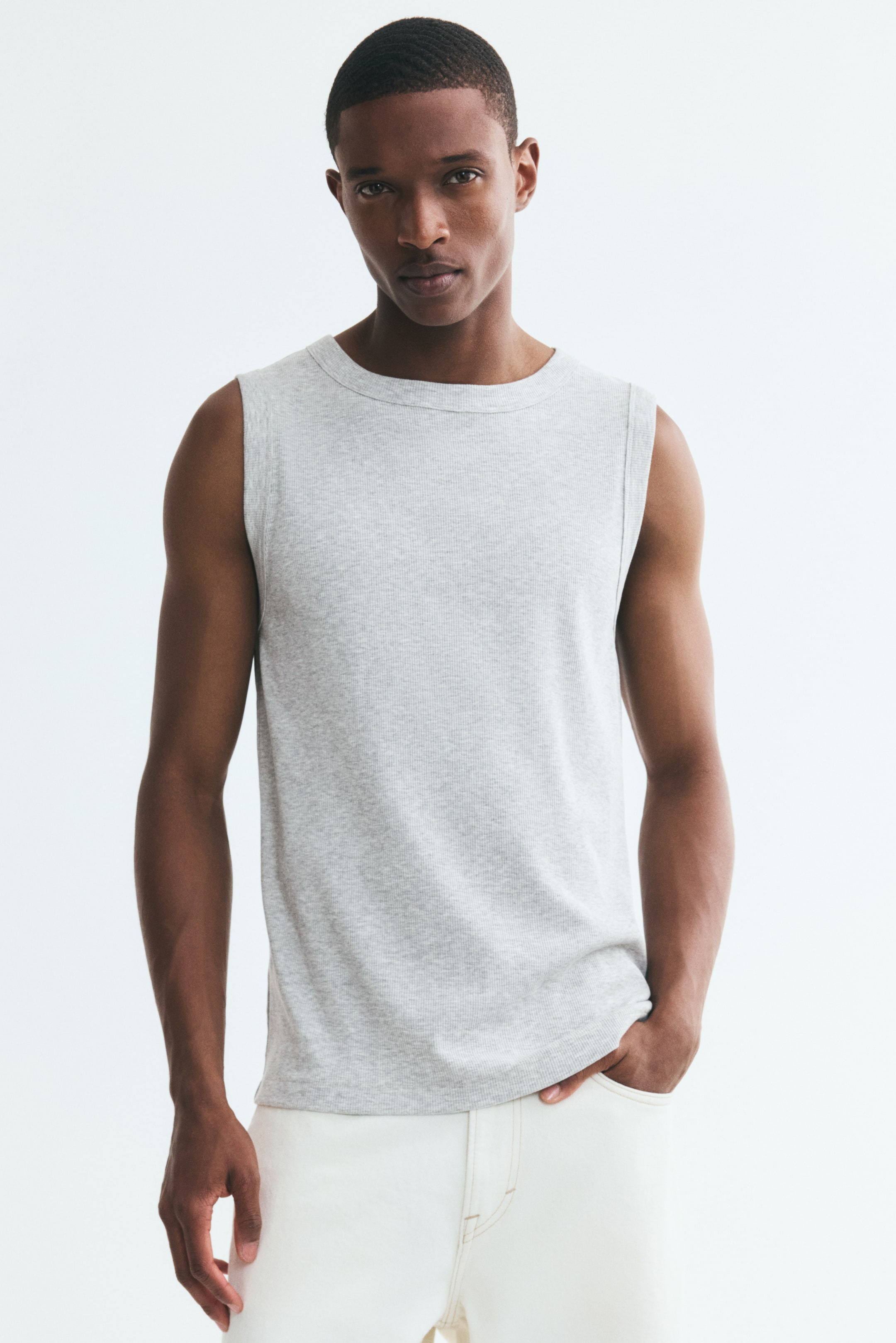 View larger image: A light gray, ribbed cotton-blend tank top featuring a round neckline and a straight-cut hem is being worn by the model. The slim-fit top is styled with cream-colored trousers, with the model resting one hand in a pocket.