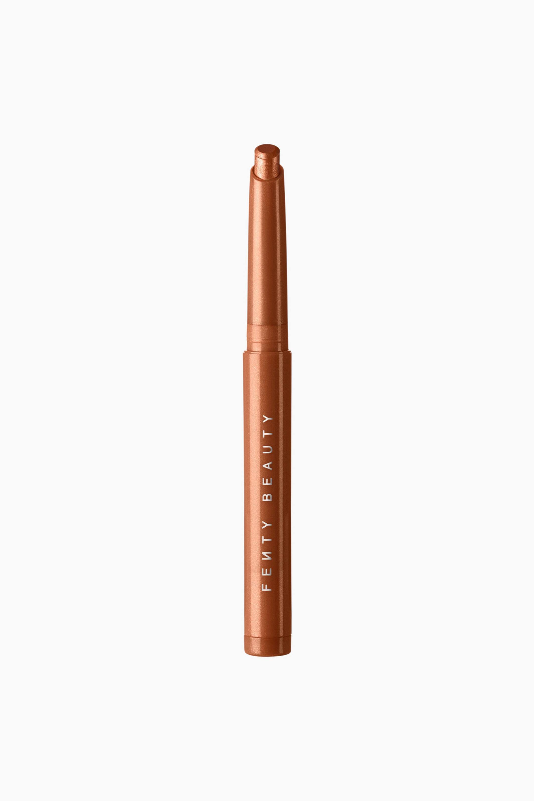 Se større billede: Shadowstix Longwear Eyeshadow Stick står lodret med et metallisk bronzefarvet hylster og det hvide "FENTY BEAUTY"-logo trykt lodret langs stangen. Hætten er fjernet, og den afrundede, metalliske bronzefarvede øjenskyggetip ses stikke frem fra toppen.