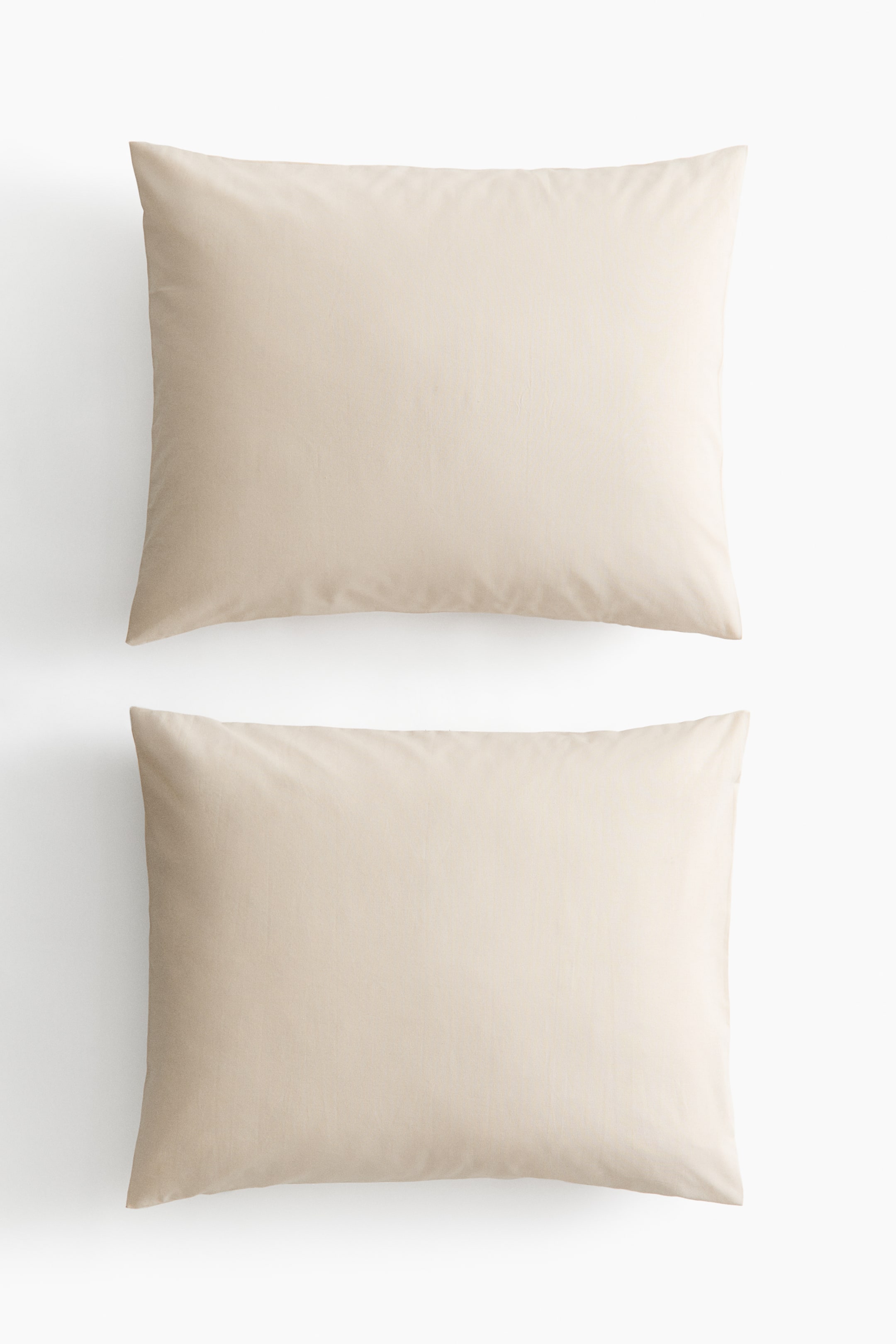 View larger image: A pair of light beige pillowcases is lying flat, presenting its front side with a smooth cotton weave texture and neatly finished rectangular edges.