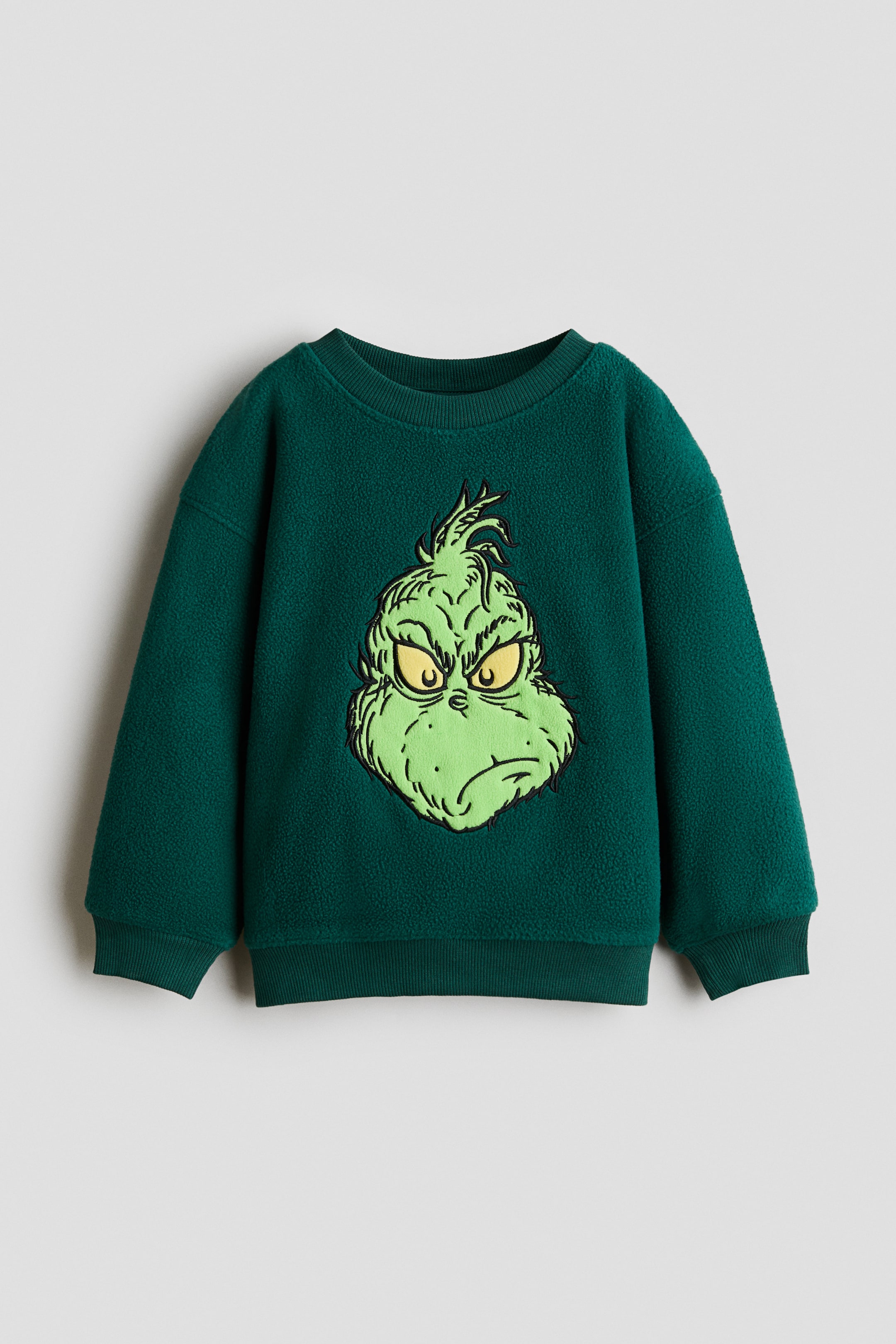 View larger image: A dark green fleece sweatshirt, front-facing, features a large central graphic of a green character with a frowning expression and yellow eyes. The sweatshirt has a ribbed crew neck, dropped shoulders, ribbed cuffs, and a ribbed hem.
