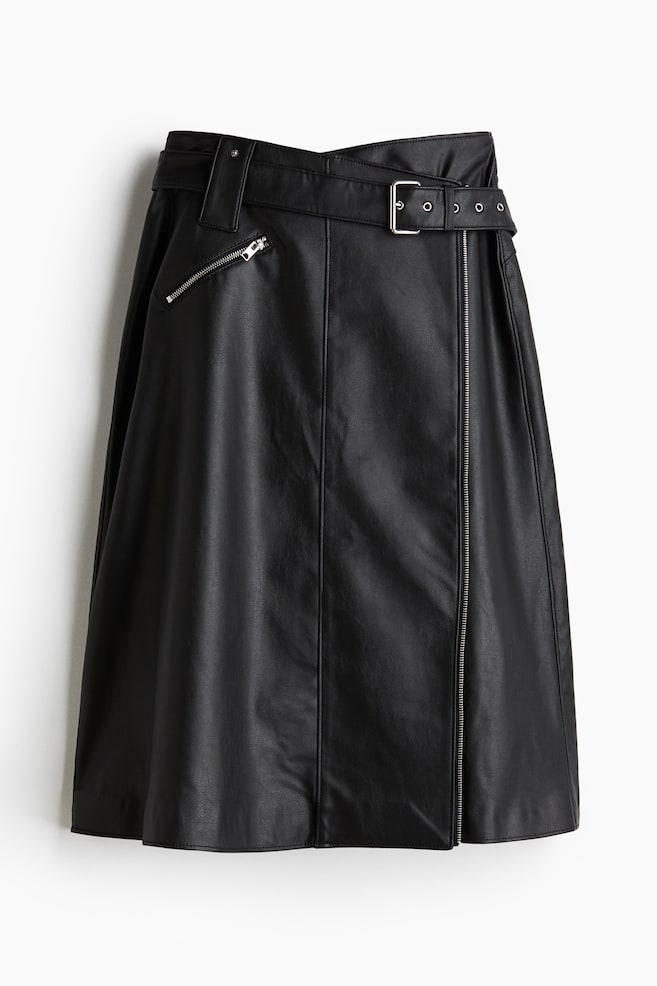 A black leather-look A-line skirt is seen from the front, featuring a matching belted waistband with a silver-tone buckle and grommets. It is displaying a diagonal silver-tone zipper pocket on the left and a long vertical silver-tone zipper detail on the right. - 1