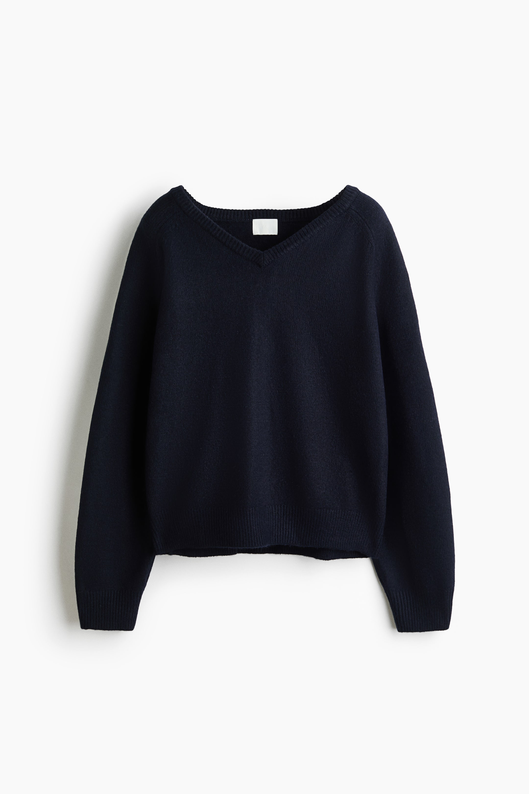 Agrandir l'image: Un pull bleu foncé à col en V est présenté de face, avec de longues manches raglan, des poignets côtelés et un ourlet côtelé. Une petite étiquette blanche est visible à l’arrière du col.