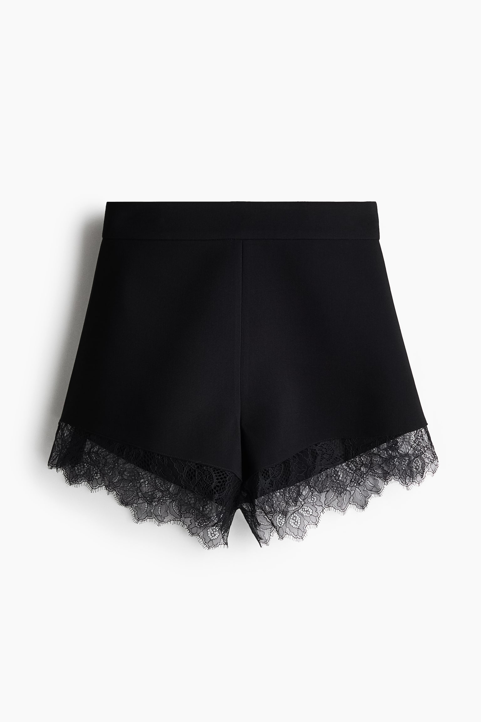 A pair of black high-waisted shorts is shown from the front, showcasing a structured silhouette with a wide, flat waistband. Delicate black lace trim with scalloped and eyelash edges details the curved leg openings.