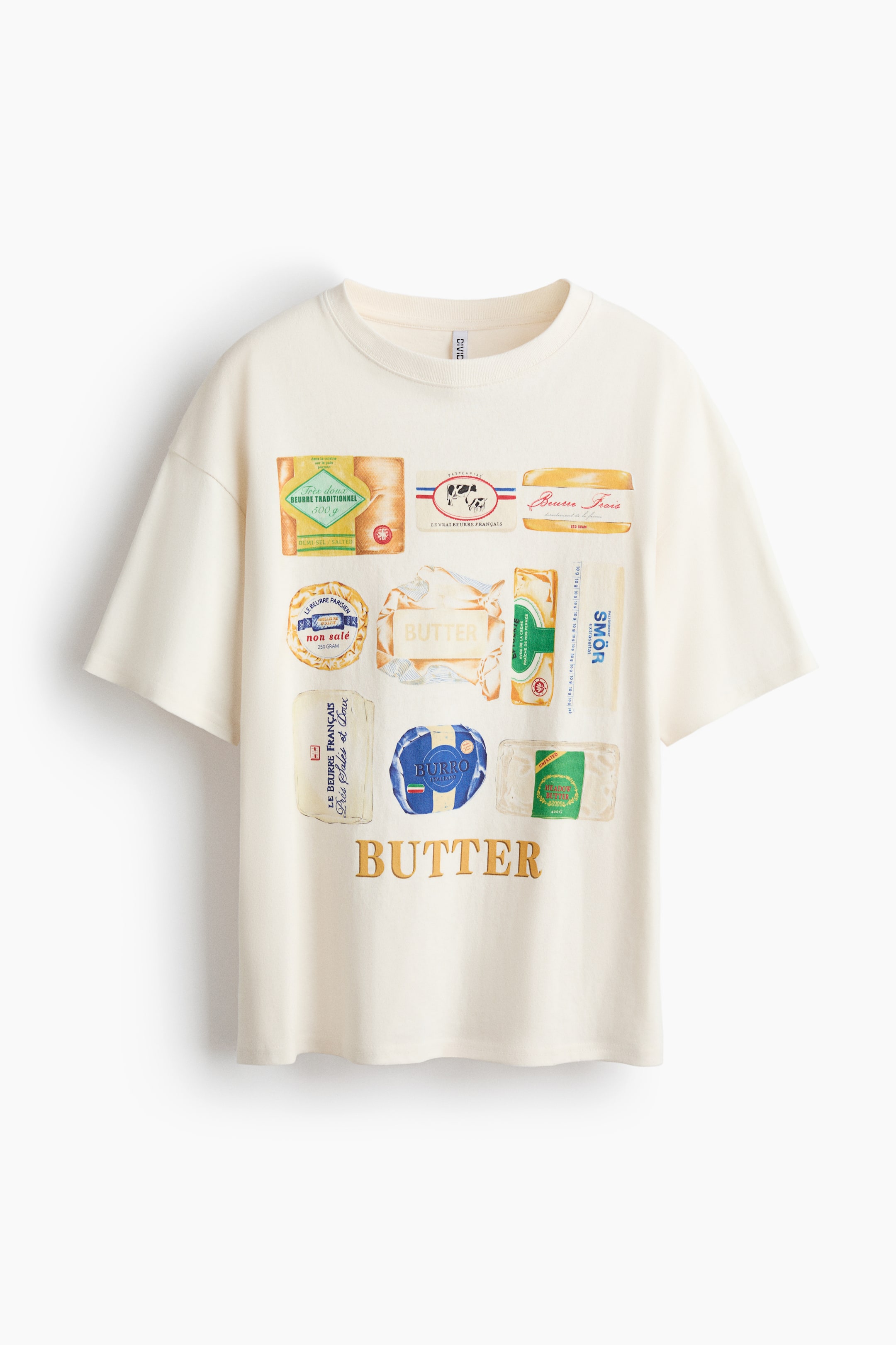 拡大画像を表示: オーバーサイズのTシャツがそのFRONTを見せています。クリーム色のジャージー生地で作られ、丸いリブ付きのネックライン、ドロップショルダー、ストレートカットの裾が特徴です。フロントには、さまざまなバターのパッケージデザインとラベルのプリントモチーフが施され、下部には『BUTTER』という金色の文字が描かれています。