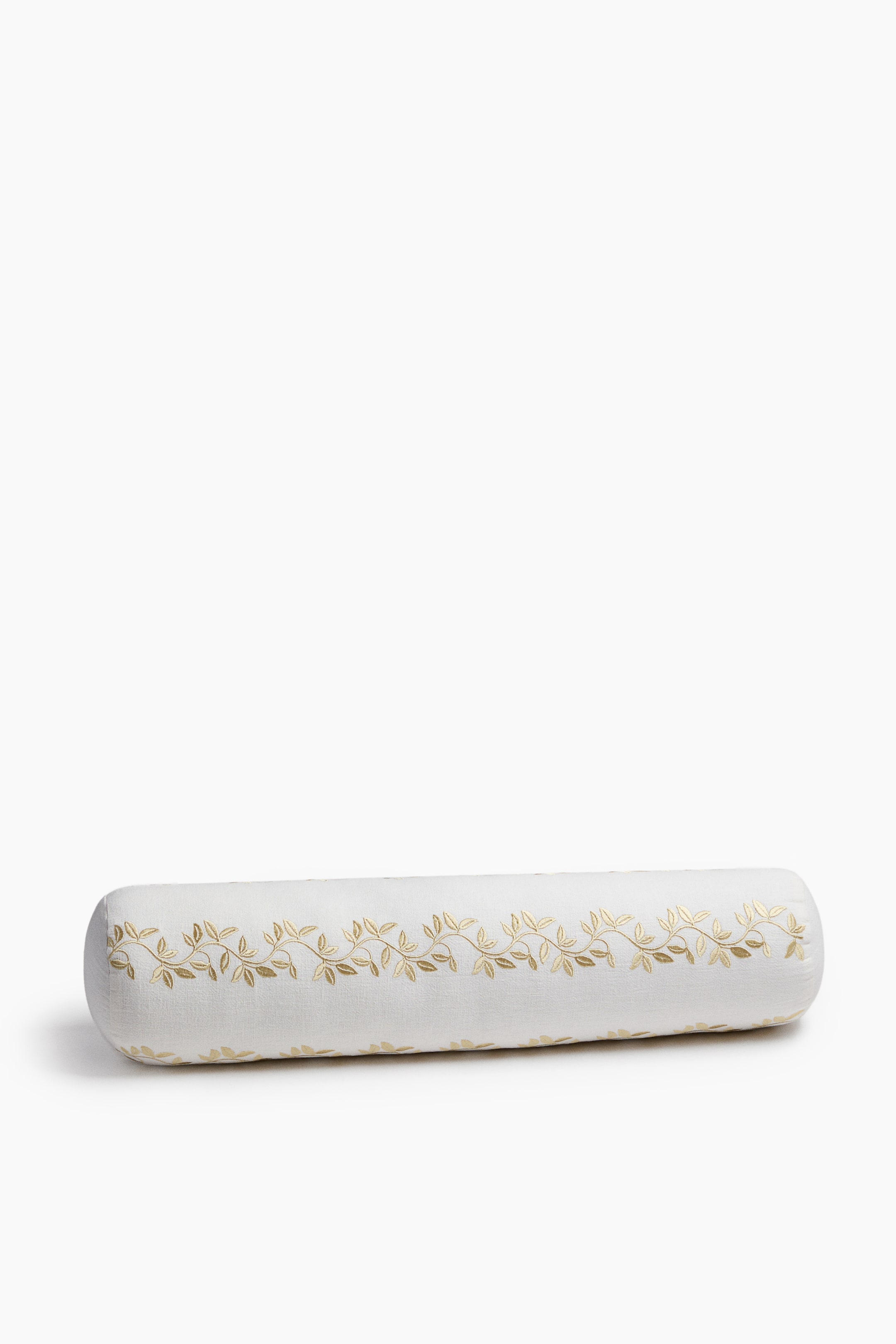 View larger image: A cylindrical bolster pillow crafted from off-white cotton and linen canvas is lying horizontally, showcasing a gold satin-stitched leafy vine motif running across its front. The bolster features rounded ends and a visible woven texture, with the detailed embroidery accentuating its elongated shape.