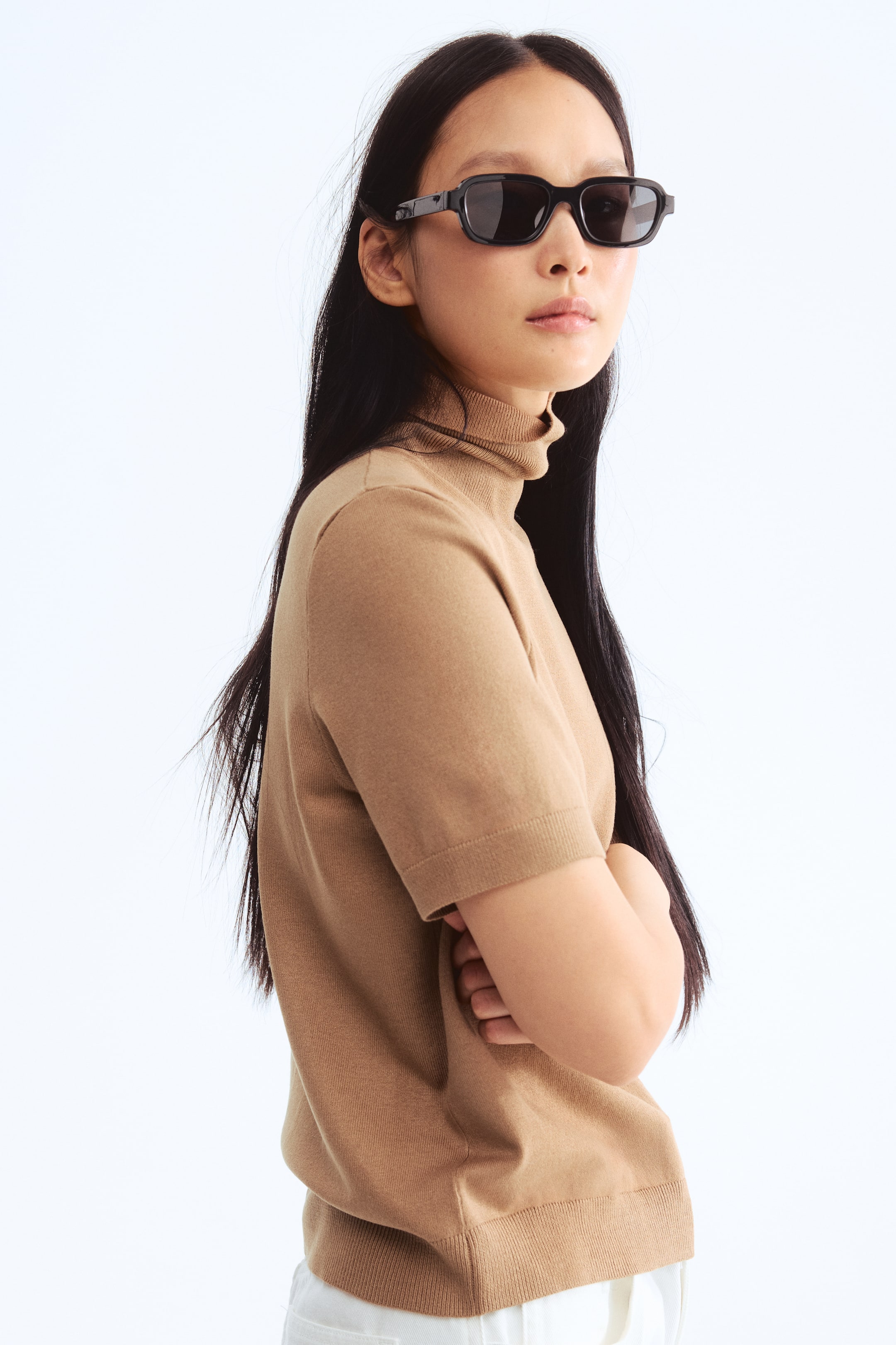 Xem ảnh lớn hơn: Một chiếc áo cổ lọ ngắn tay màu nâu nhạt đang được trình bày từ góc nhìn bên cạnh, có cổ lọ gân, tay ngắn và lai gân với kết cấu đan mịn.