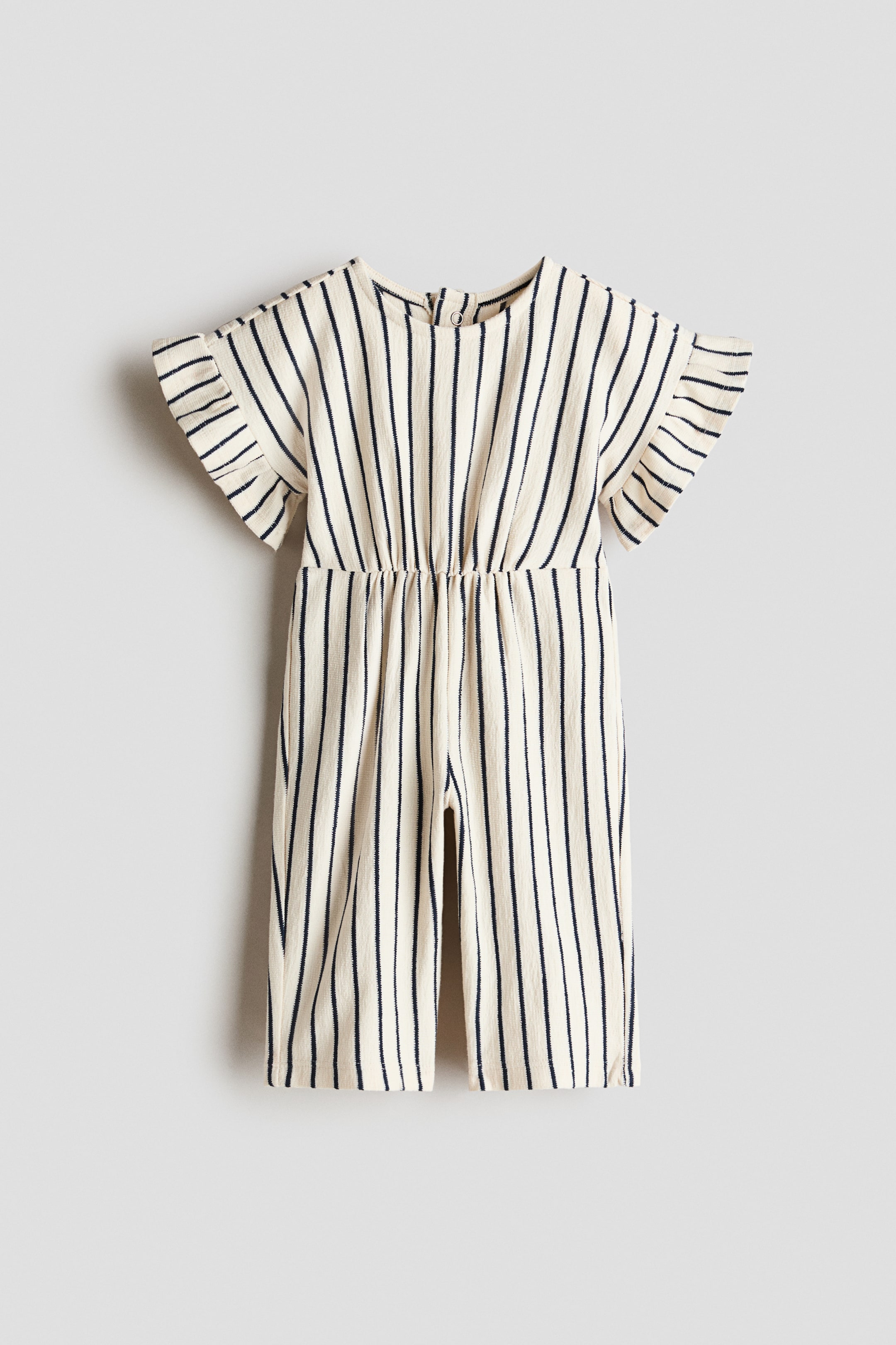 View larger image: The romper suit is displayed from the back, showcasing an off-white textured jersey with black vertical stripes. It features a round neckline, a snap-button opening at the back, flutter sleeves, gathered elastic at the waist, and long legs.