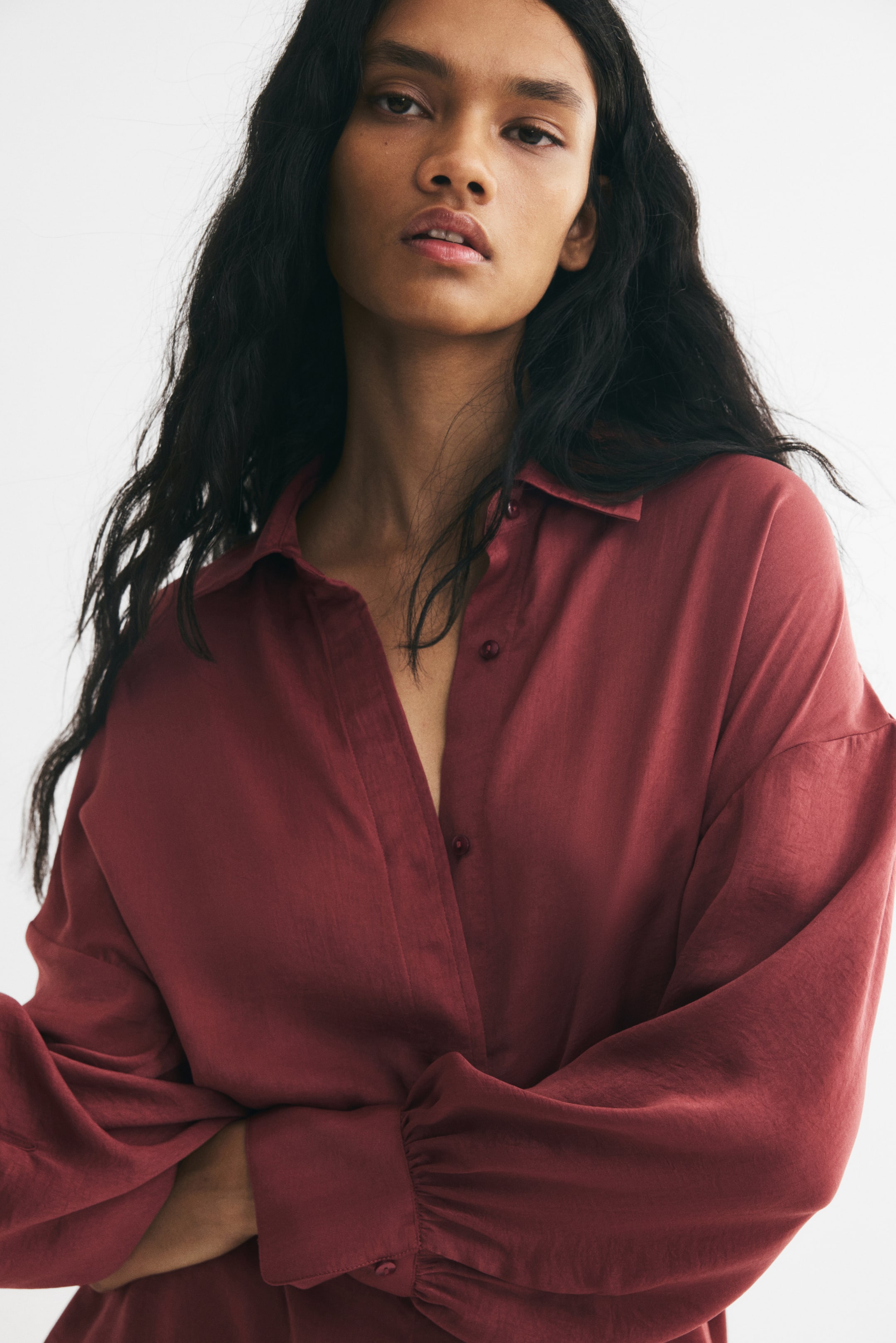 View larger image: The model is wearing a dark red shirt in a lightly crinkled weave with a slight sheen. The shirt features a collar, dropped shoulders, and long balloon sleeves with button cuffs.