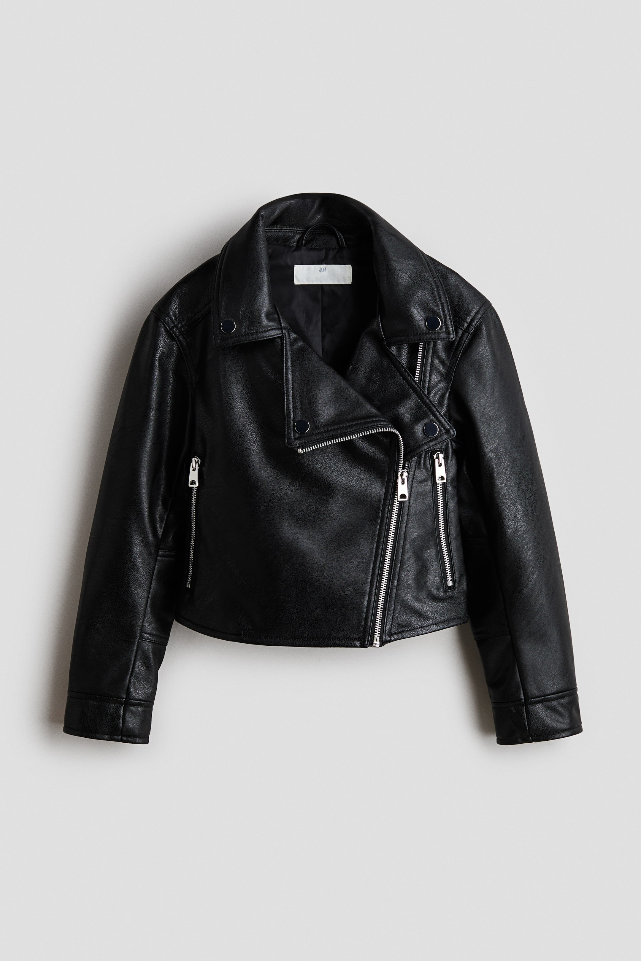 View larger image: A black faux leather jacket is presenting its front, featuring wide notched lapels with snap buttons and an asymmetrical silver-toned zipper closure. It is also displaying two zipped pockets at the waist, one zipped chest pocket, and long sleeves with zipped cuffs.