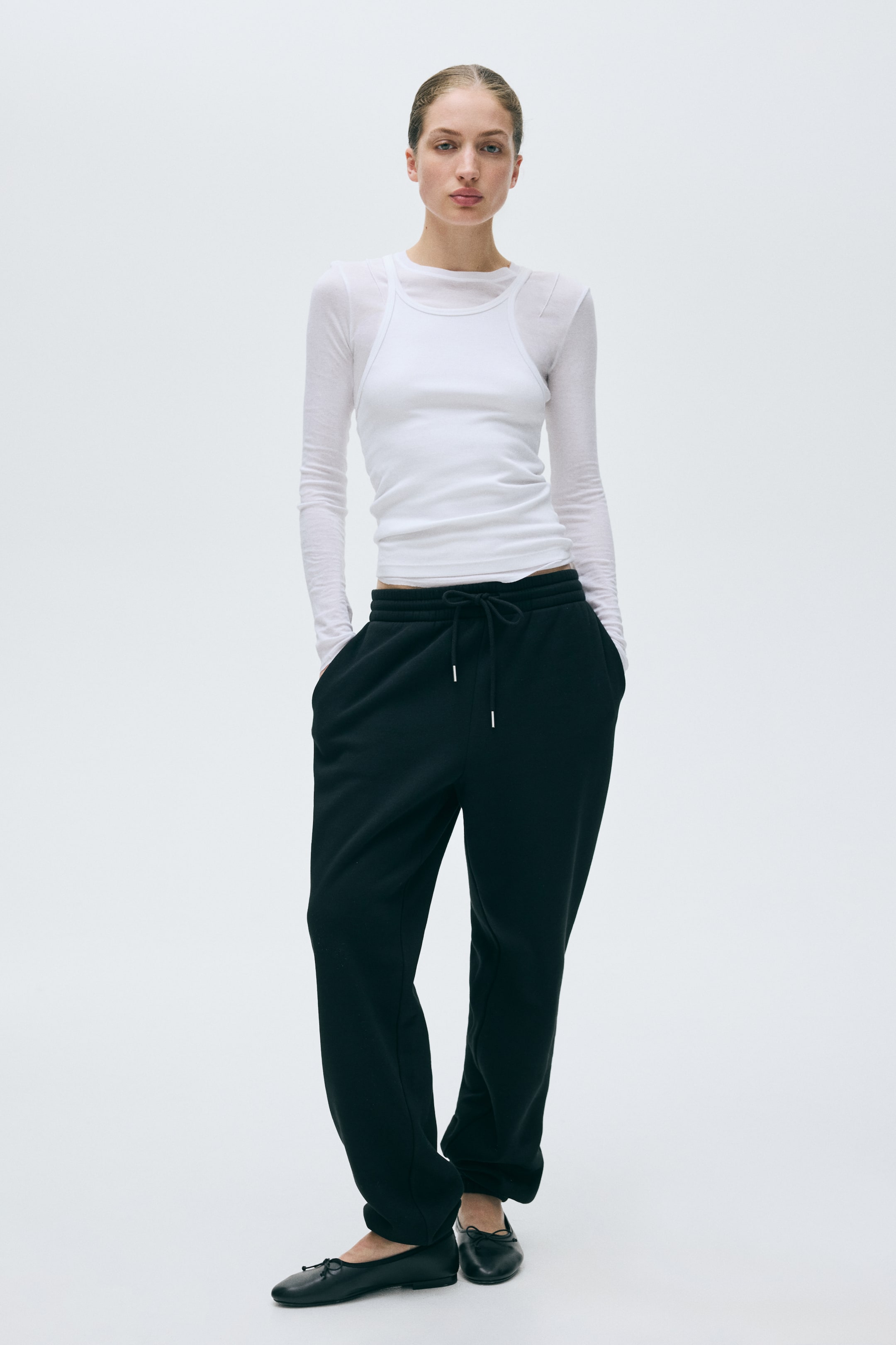 View larger image: Black sweatpants featuring a relaxed, full-length fit. They showcase an elastic waistband, a tied drawstring with silver-toned tips, and side pockets.