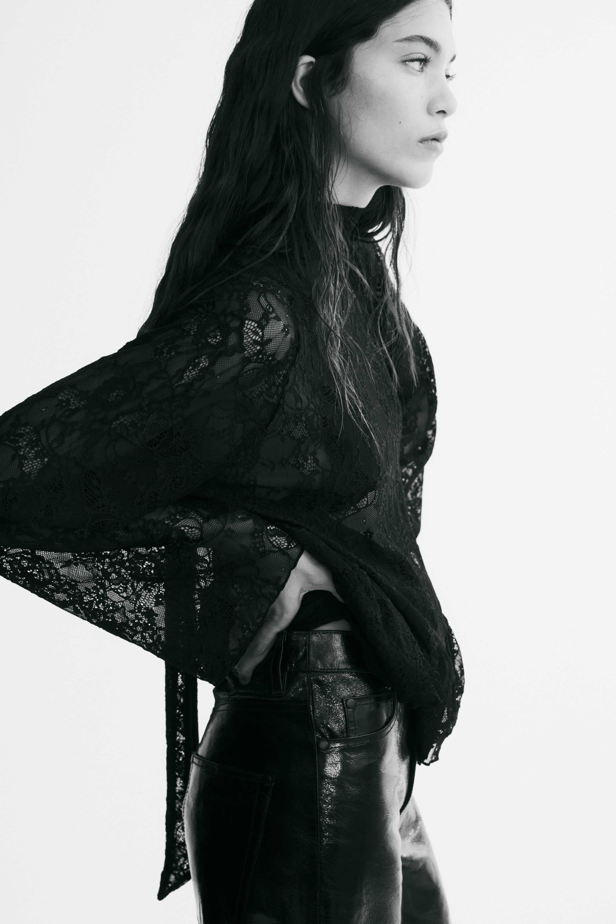 A black, loose-fit blouse in sheer lace is shown facing front, featuring a high stand-up collar, long raglan sleeves, and a wide, double-layered flounce at the hem.