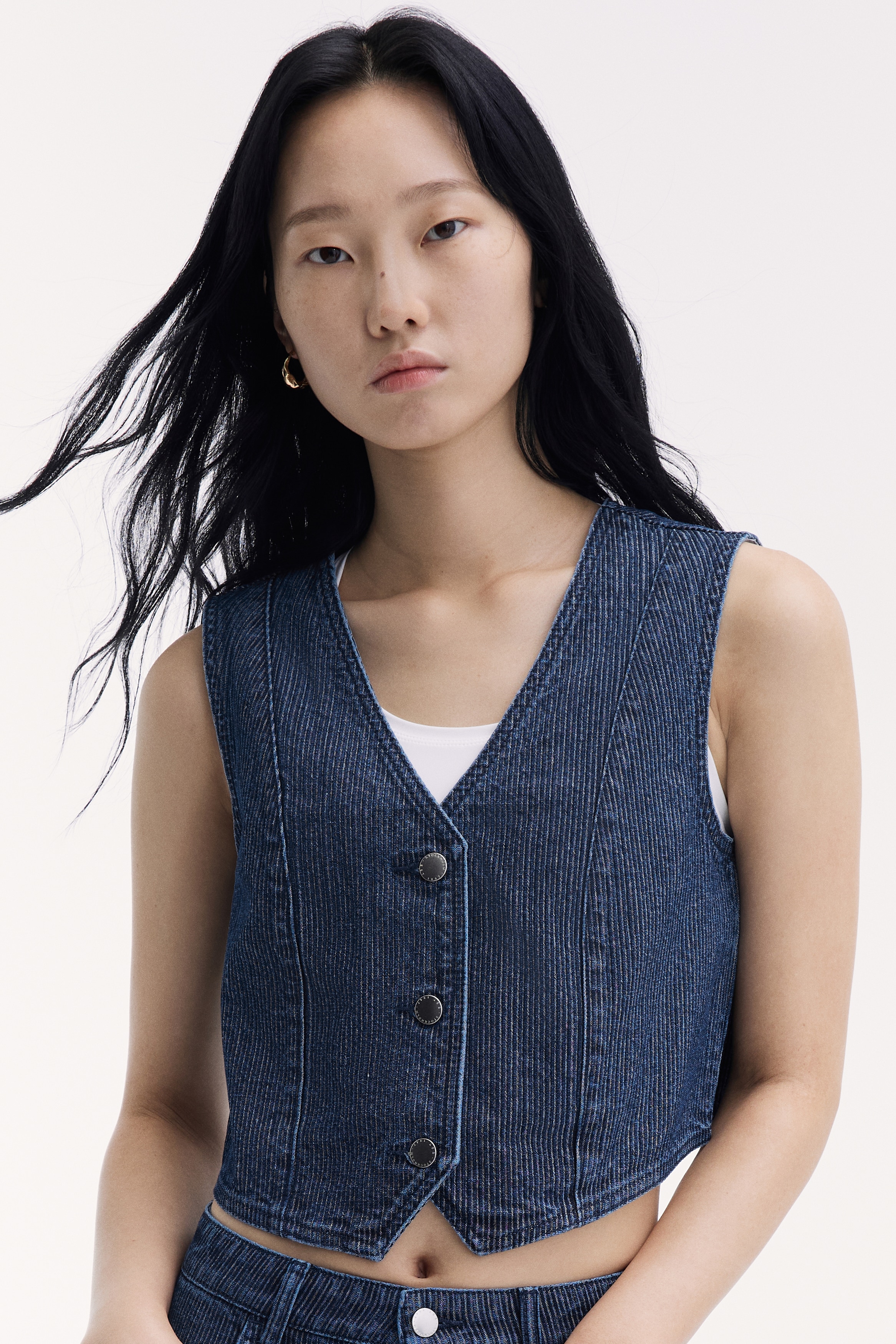 Chiáº¿c Ã¡o gile denim xanh Äáº­m, chá»¥p chÃ­nh diá»n nÃ y ná»i báº­t vá»i há»a tiáº¿t sá»c káº» dá»c vÃ  pháº§n cá» chá»¯ V cá» Äiá»n. Thiáº¿t káº¿ cÃ³ khÃ³a cÃ i phÃ­a trÆ°á»c gá»m ba nÃºt vá»i nÃºt mÃ u báº¡c, chi tiáº¿t ÄÆ°á»ng may ghÃ©p máº£ng vÃ  váº¡t trÆ°á»c nhá»n.