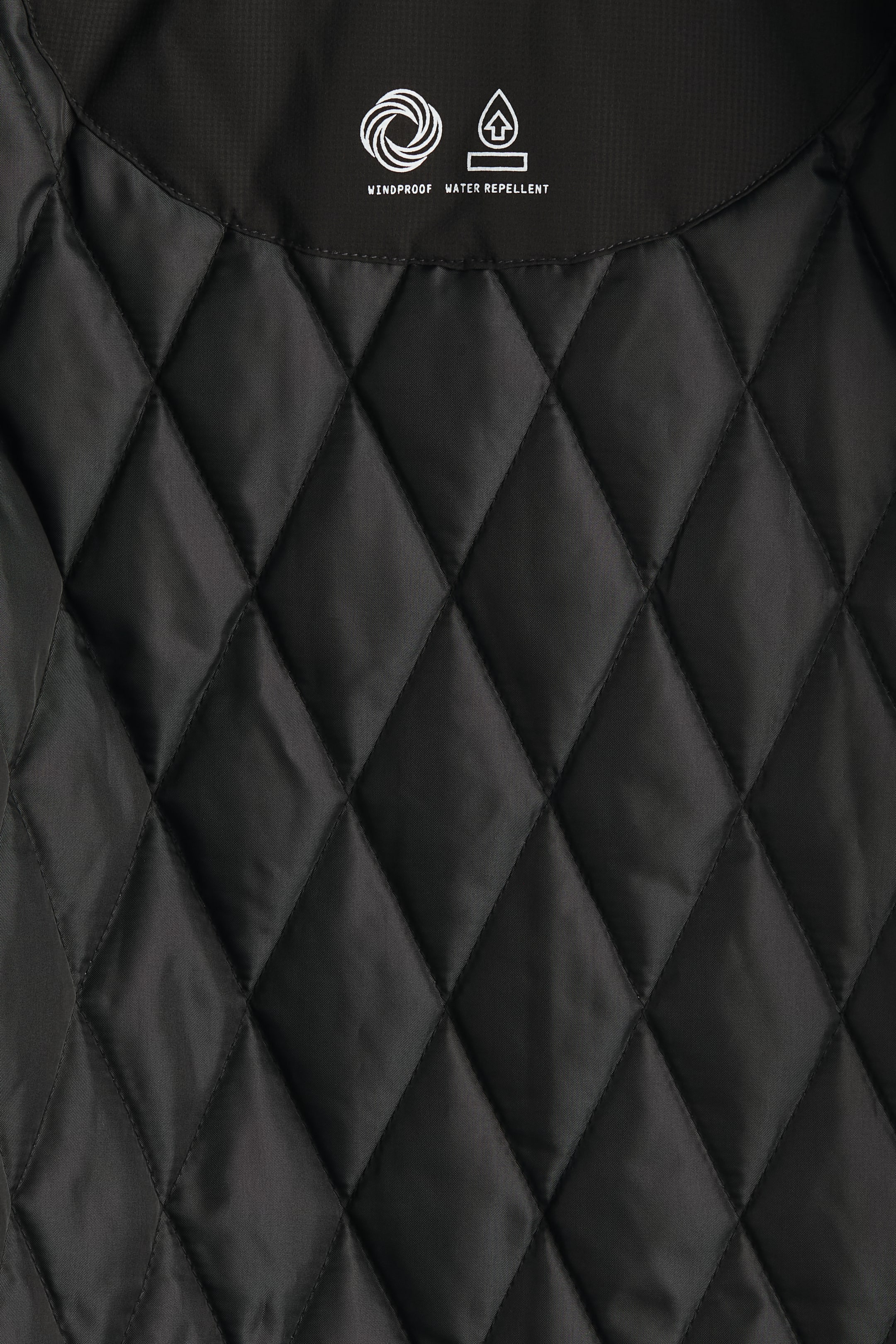 이미지 확대 보기: 검정색 퀼트 안감에는 전체적으로 다이아몬드 패턴이 있습니다. 윗면의 매끄러운 패널에는 "WINDPROOF" 및 "WATER REPELLENT" 속성을 나타내는 흰색 아이콘과 텍스트가 표시됩니다.