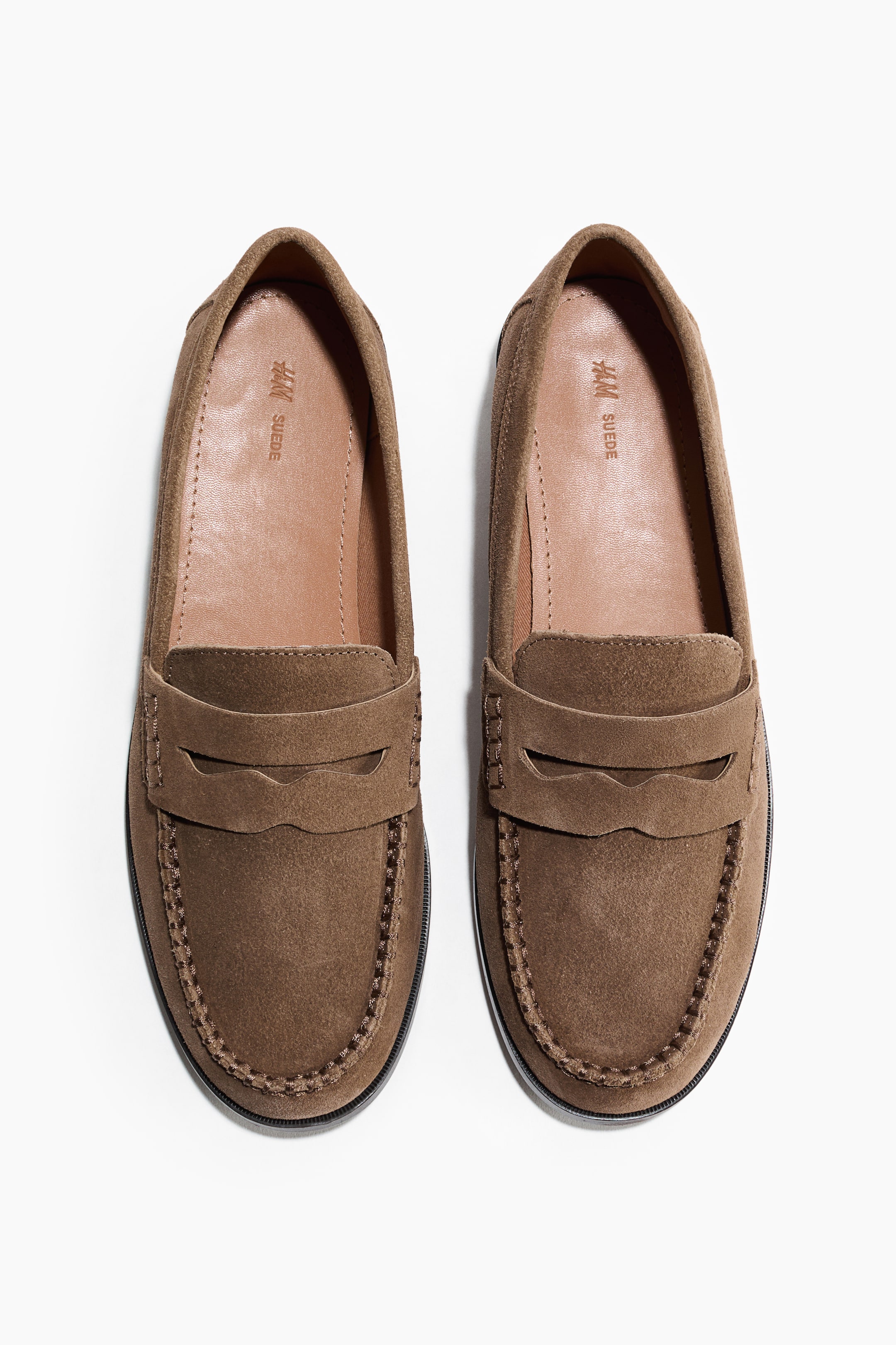 View larger image: A pair of brown suede penny loafers is showcasing moccasin-style stitching around the toe and a penny strap with a cut-out across the vamp. The light brown interior lining is embossed with "H&M SUEDE".