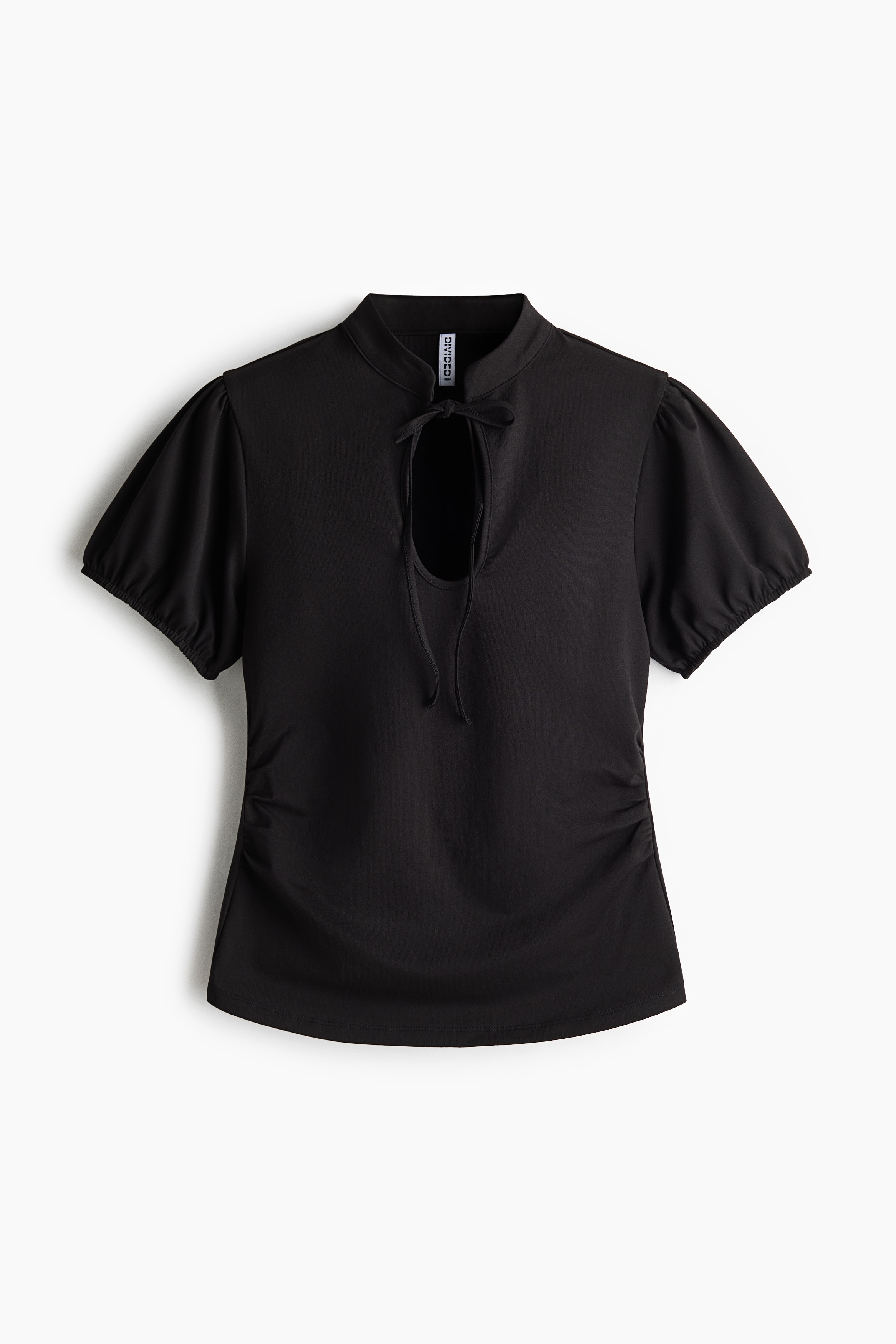 La modelo lleva una camiseta ajustada de punto negro, con cuello mao, abertura frontal tipo lÃ¡grima con lazos finos, mangas cortas abullonadas y costuras fruncidas en los laterales a la altura de la cintura. La prenda se combina con una falda de cuero negro y un cinturÃ³n de cadena con discos plateados.