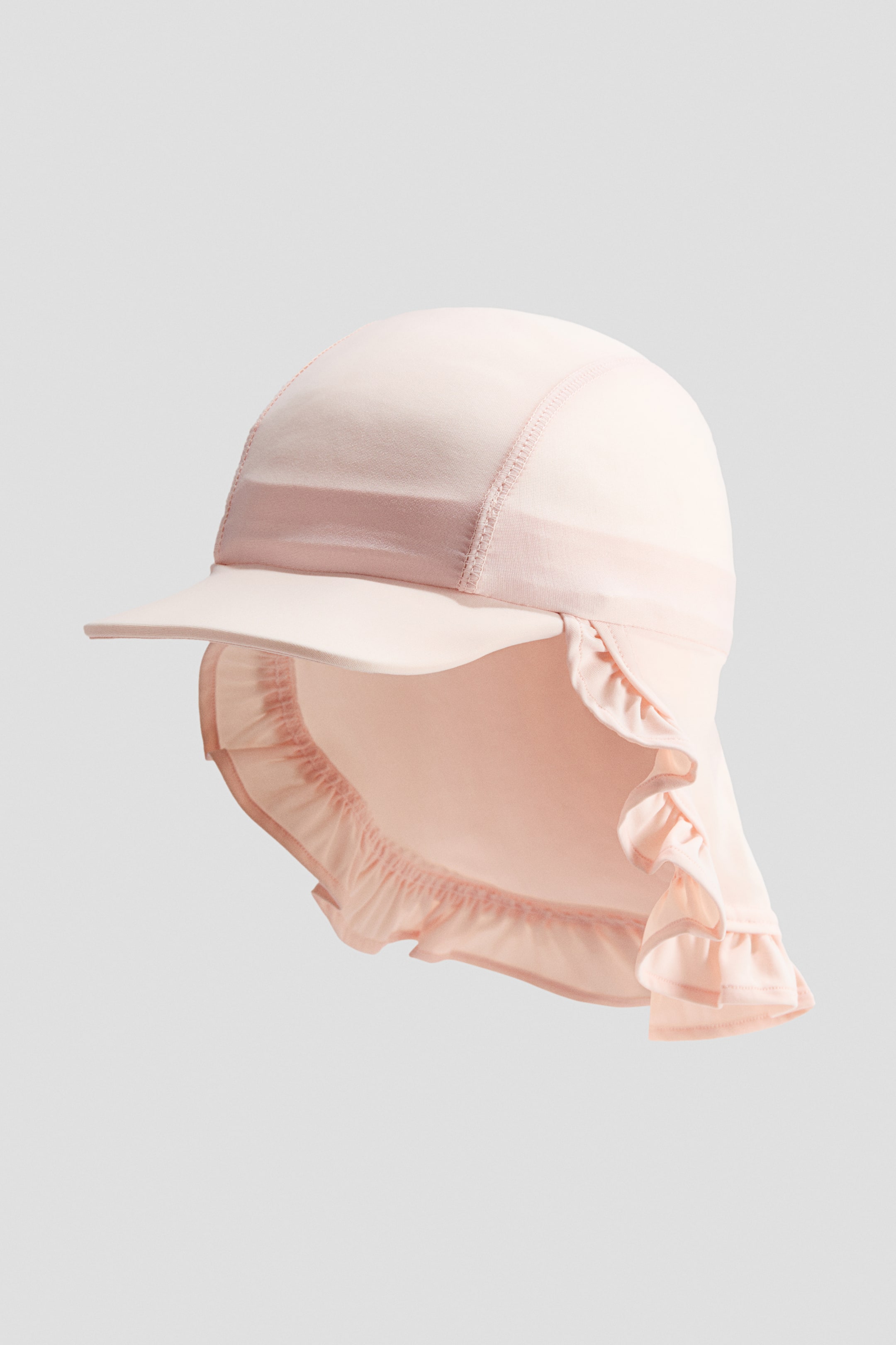 View larger image: The sun cap in a soft pink hue boasts a sturdy peak at the front, complemented by an elegantly ruffled neck flap extending at the back. Noticeable seam lines adorn the crown of the cap, while the neck flap's top edge features elastic gathering for a snug fit.