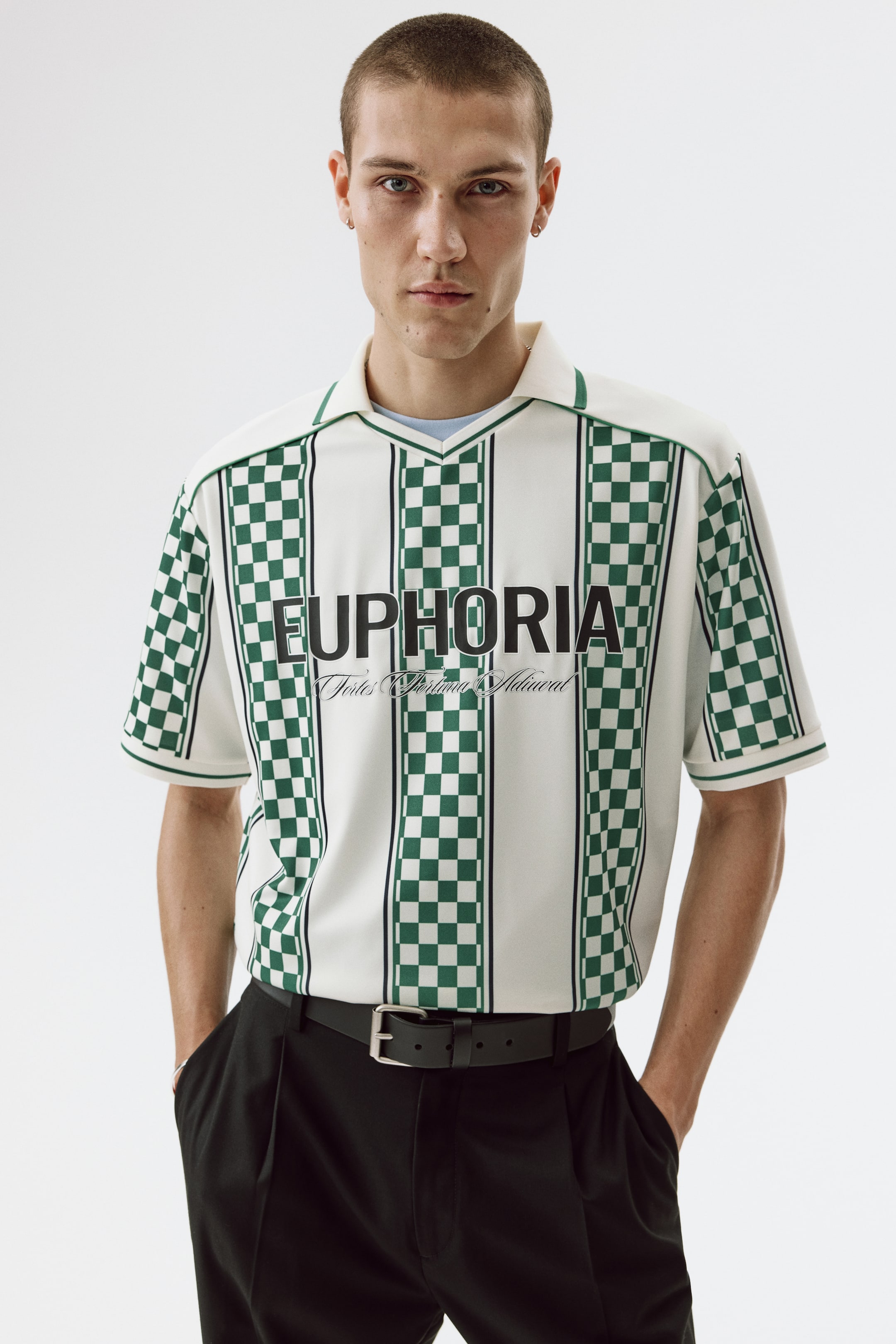 View larger image: The short-sleeved shirt showcases a cream base with vertical stripes alternating between cream and green checkerboard patterns. It is complemented by a green-trimmed V-neck collar and green checkerboard sleeves. The front displays "EUPHORIA" in black text with smaller stylized text beneath, and the shirt is worn tucked into black trousers.