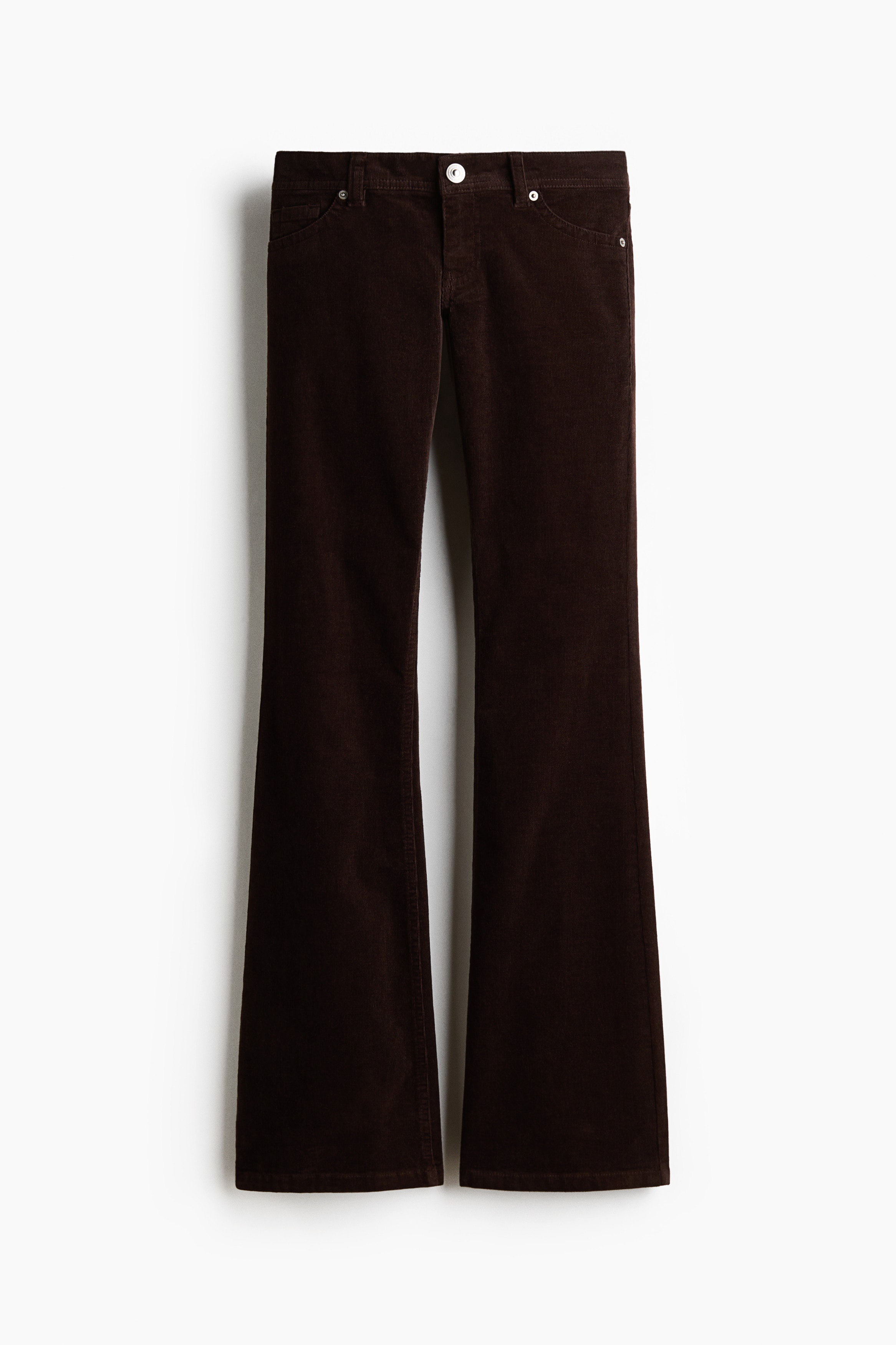 Fitted dark brown pants featuring an extra low waist, a visible coin pocket, and flared legs are being worn by the model standing in profile. The pants are styled with a matching short-sleeved brown t-shirt and chunky dark boots.