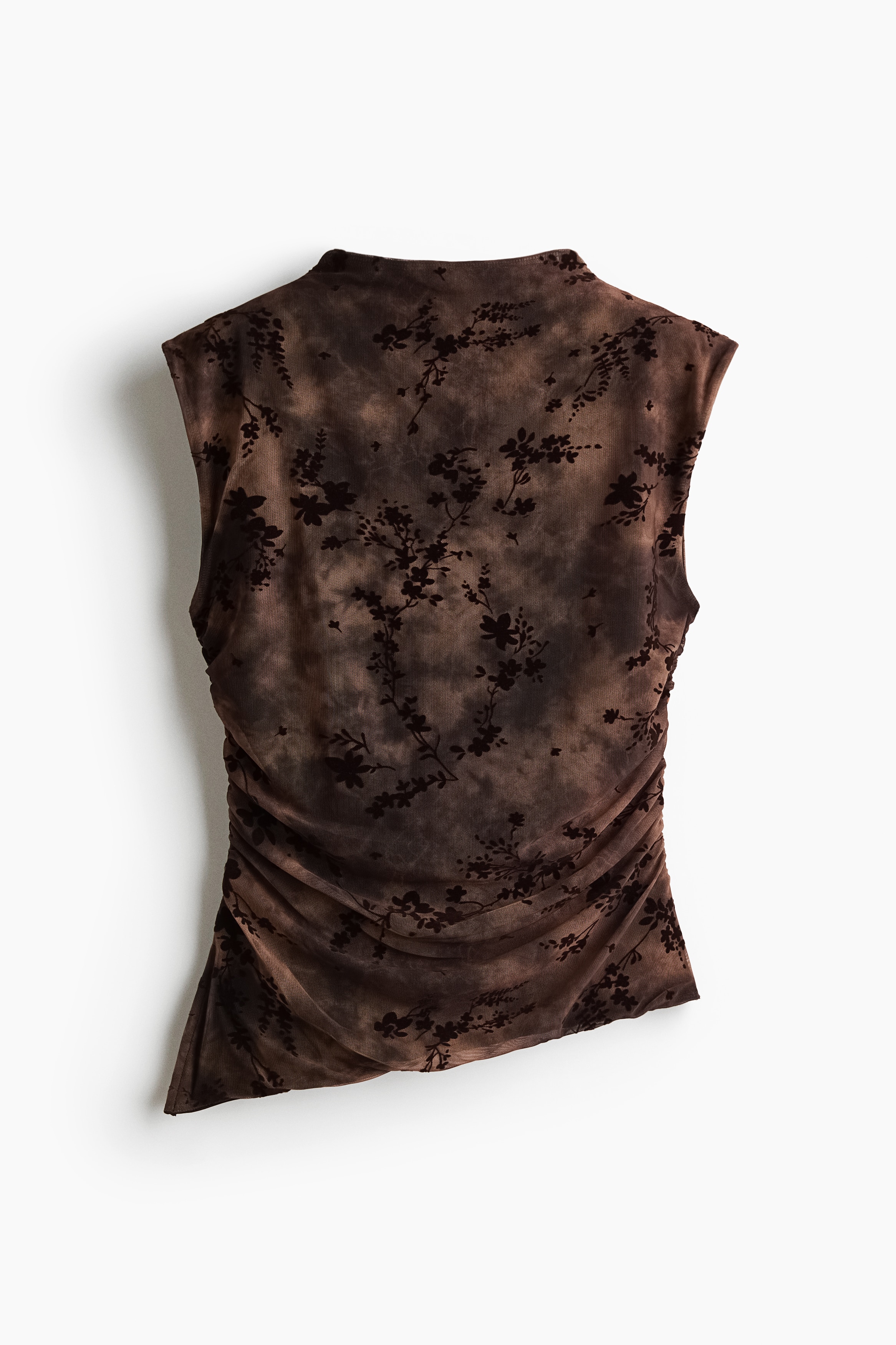 A sleeveless, fitted mesh top in a brown tie-dye pattern with a black floral flock print is worn by the model. The top features a high neck, gathered side seams, and an asymmetrical hem, and is styled with a black faux-leather skirt.