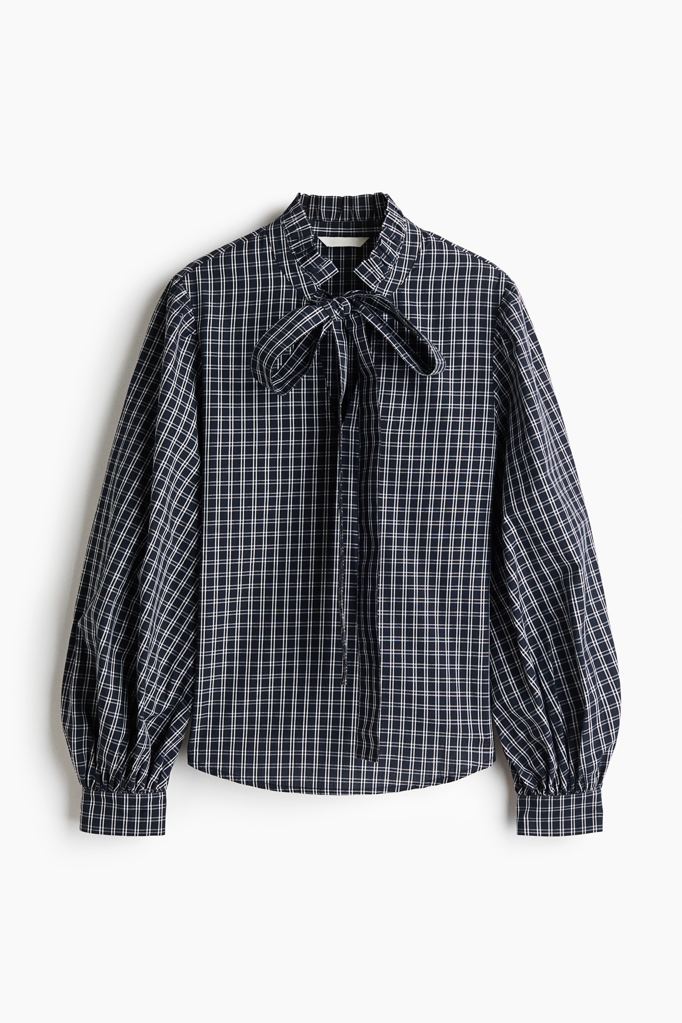 A dark, plaid-patterned blouse is being worn by the model, featuring a high collar with frill trim. The blouse has a front keyhole opening tied with a bow, and long sleeves with gathered shoulders.