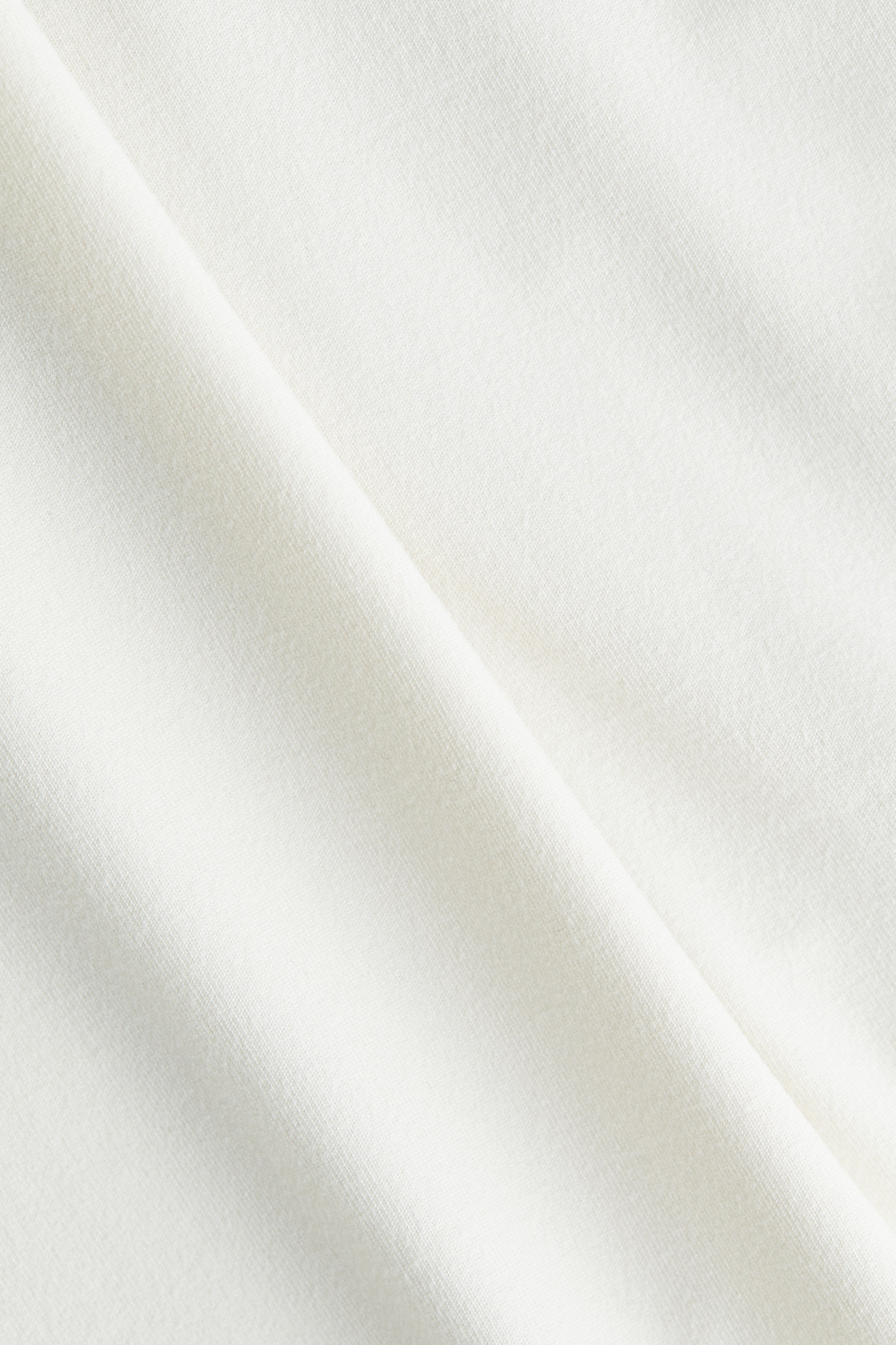 View larger image: A cream-colored fabric is being presented, featuring a subtle, fine knit texture and a prominent diagonal fold.