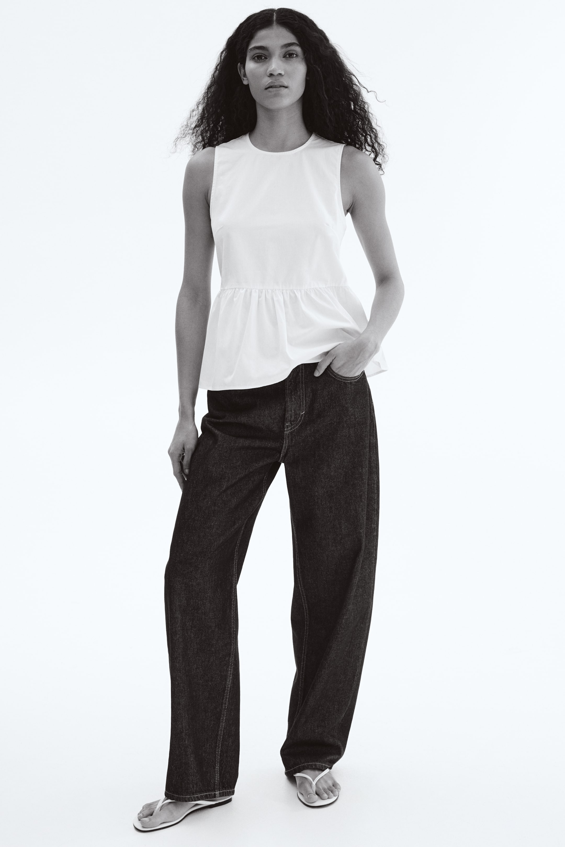 View larger image: "A white sleeveless peplum top, featuring a round neckline and a gathered waist, is being showcased from a front-facing angle, paired with dark, wide-leg jeans highlighted by visible contrast stitching."