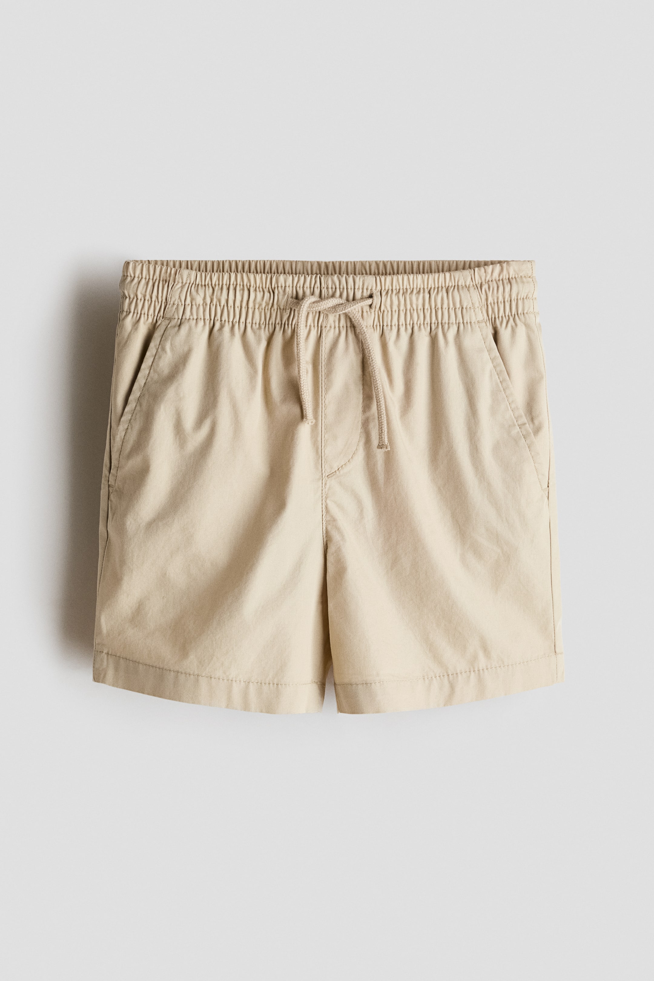 View larger image: Shorts in a soft cotton weave are being showcased from the front, featuring an elasticated, drawstring waist, a mock fly, and diagonal side pockets.