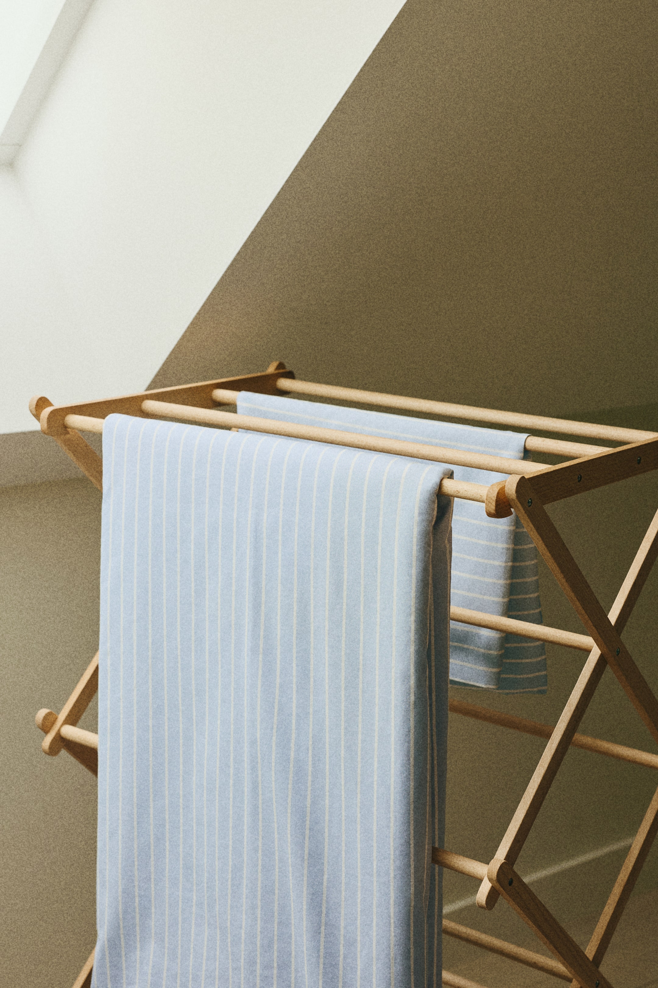 View larger image: A light blue fabric with thin white vertical stripes is draped over the wooden rods of a drying rack, hanging vertically and displaying its full pattern.