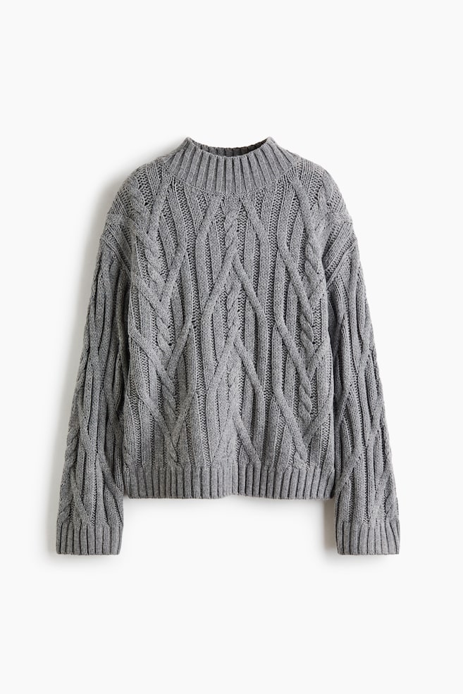 Un jersey de punto trenzado gris está orientado hacia el frente y muestra un intrincado patrón integral de ochos trenzados. El jersey presenta un cuello alto ribeteado, mangas largas de corte relajado con puños ribeteados y un bajo ribeteado. - 1