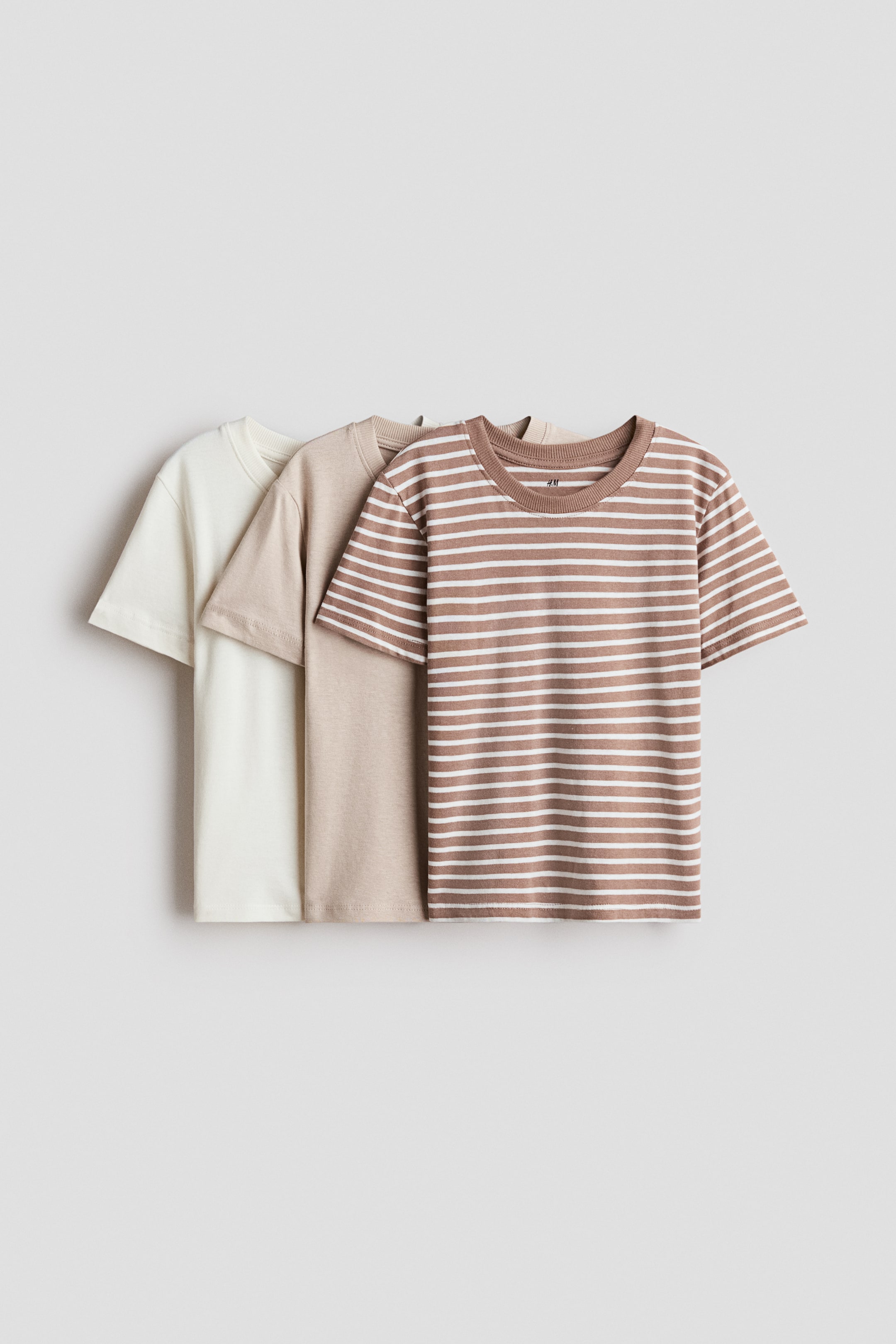 View larger image: Three cotton jersey T-shirts are overlapping each other, facing front, displaying a brown tee with horizontal white stripes, a solid light beige tee, and a solid off-white tee. Each T-shirt features a round, rib-trimmed neckline and short sleeves.